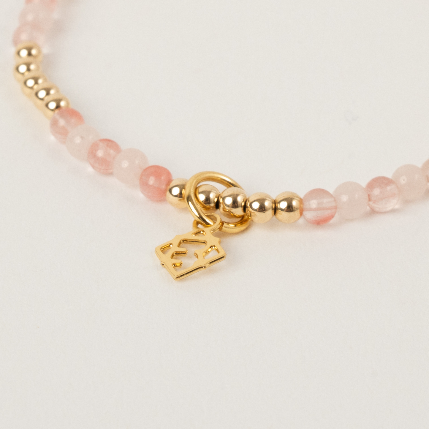 Bracelet with pink beads and gold charm on a light background