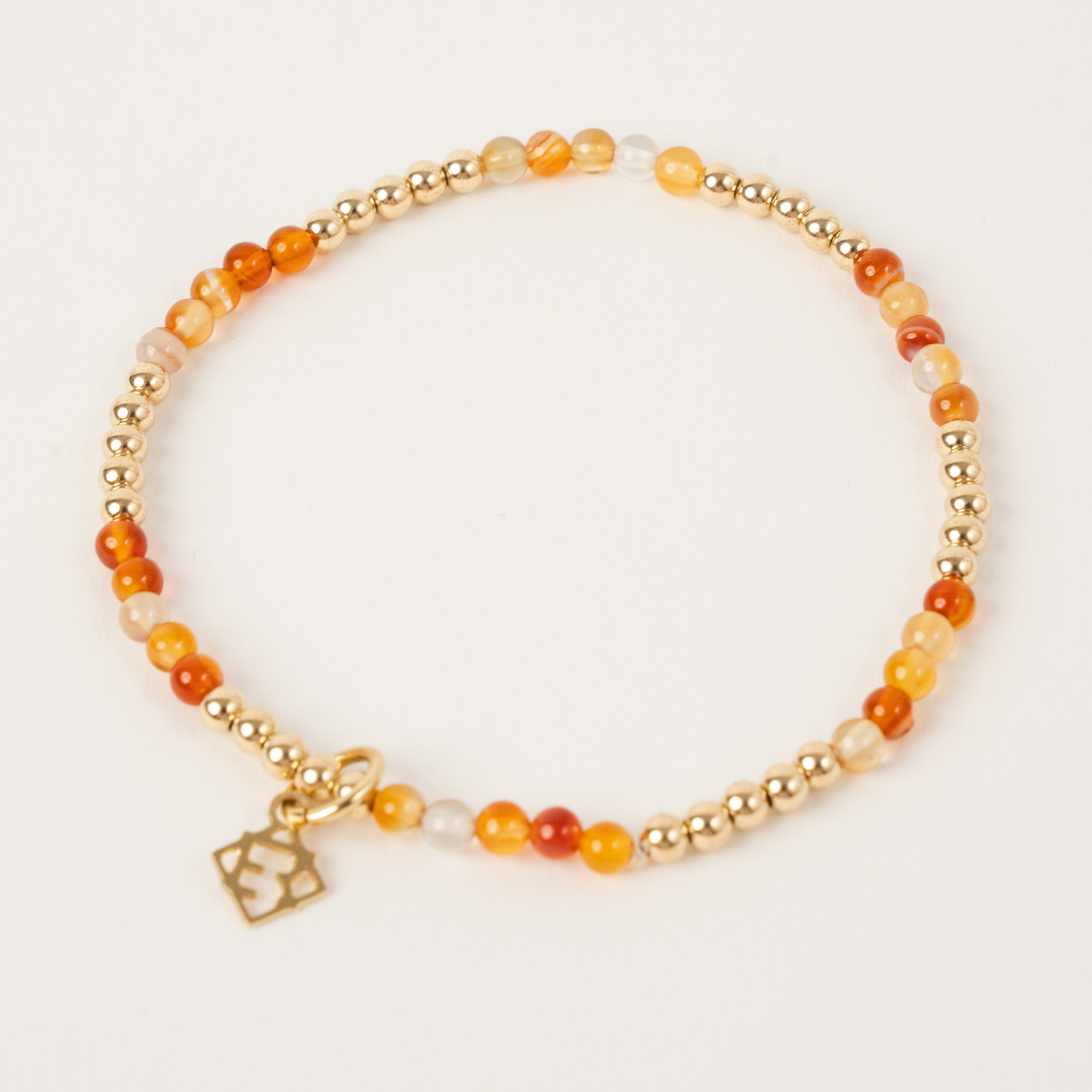 Bracelet with orange beads and gold charm on a white background