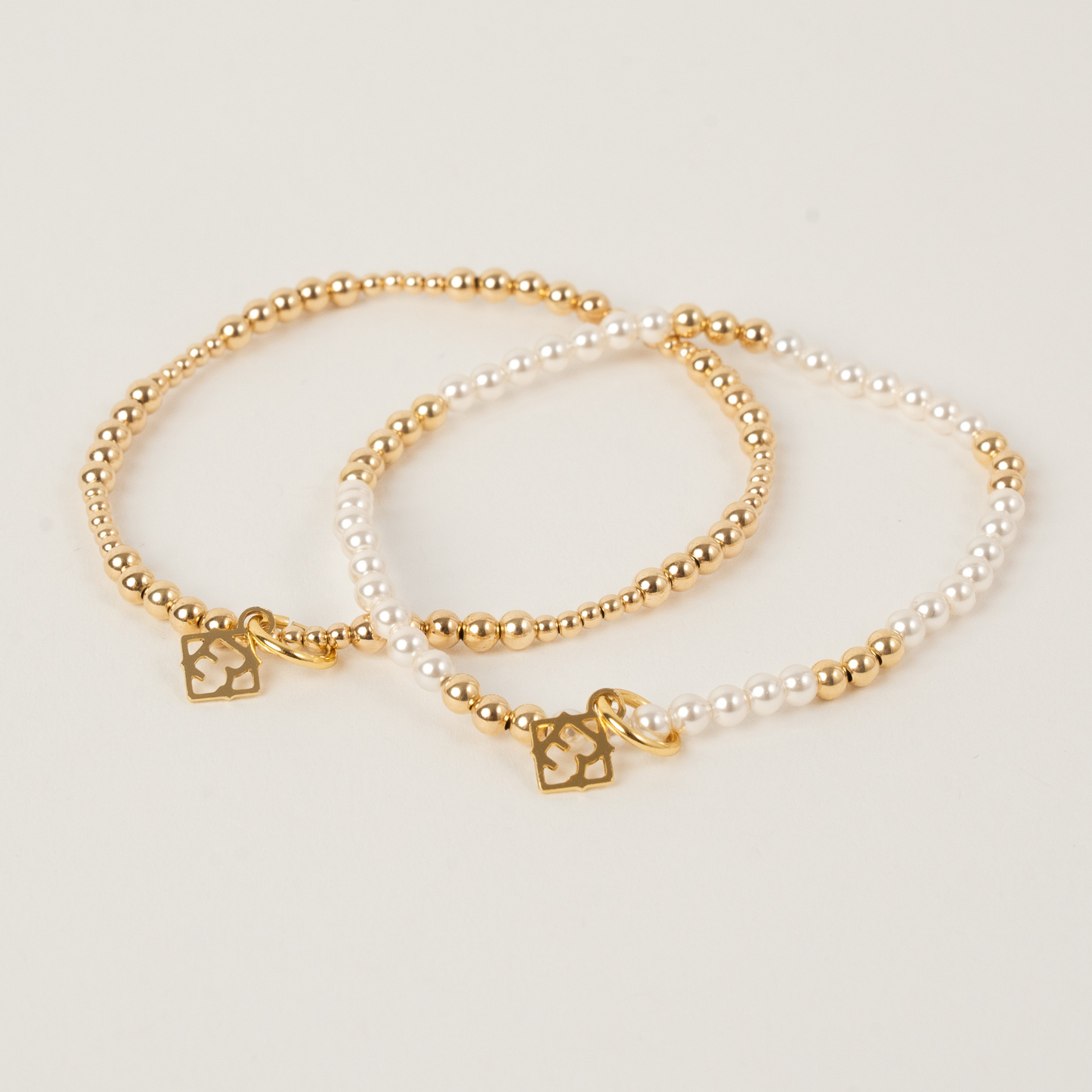 Two pearl and gold bracelets on a light background