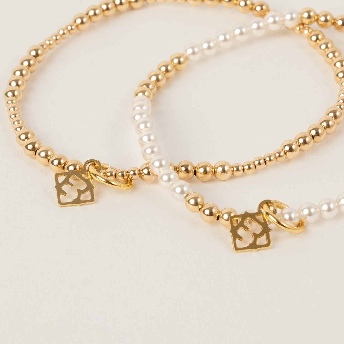 Two gold beaded bracelets with charms on a light background