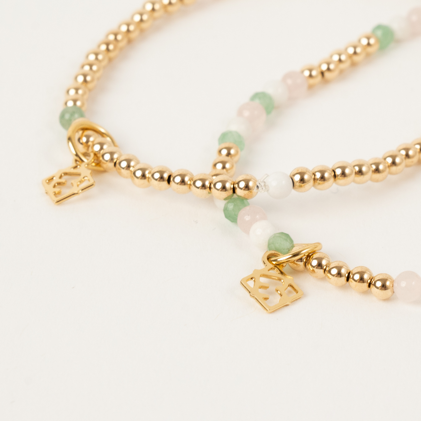 Gold beaded bracelet with green and white beads on a light background
