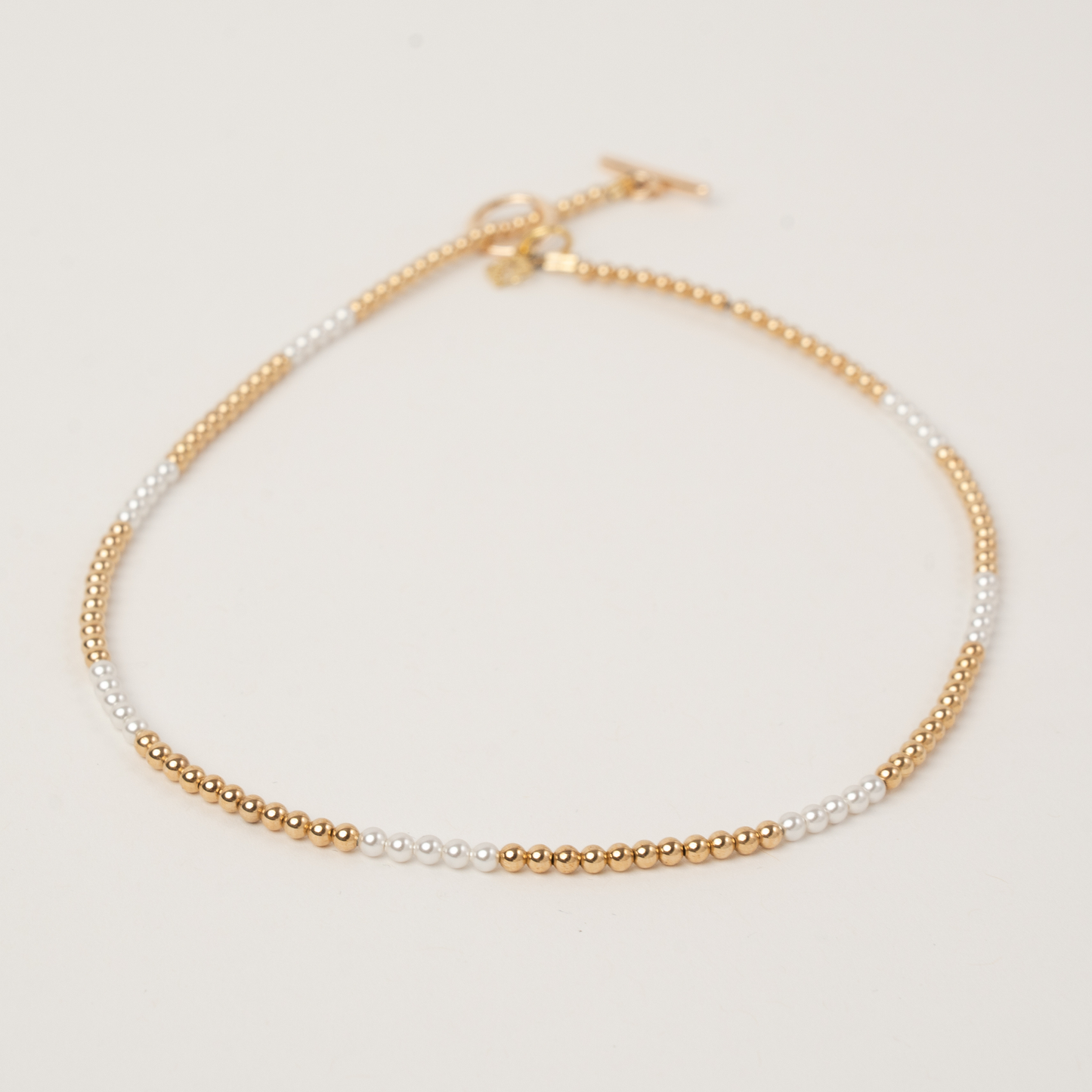 Gold and white beaded necklace on a light gray background