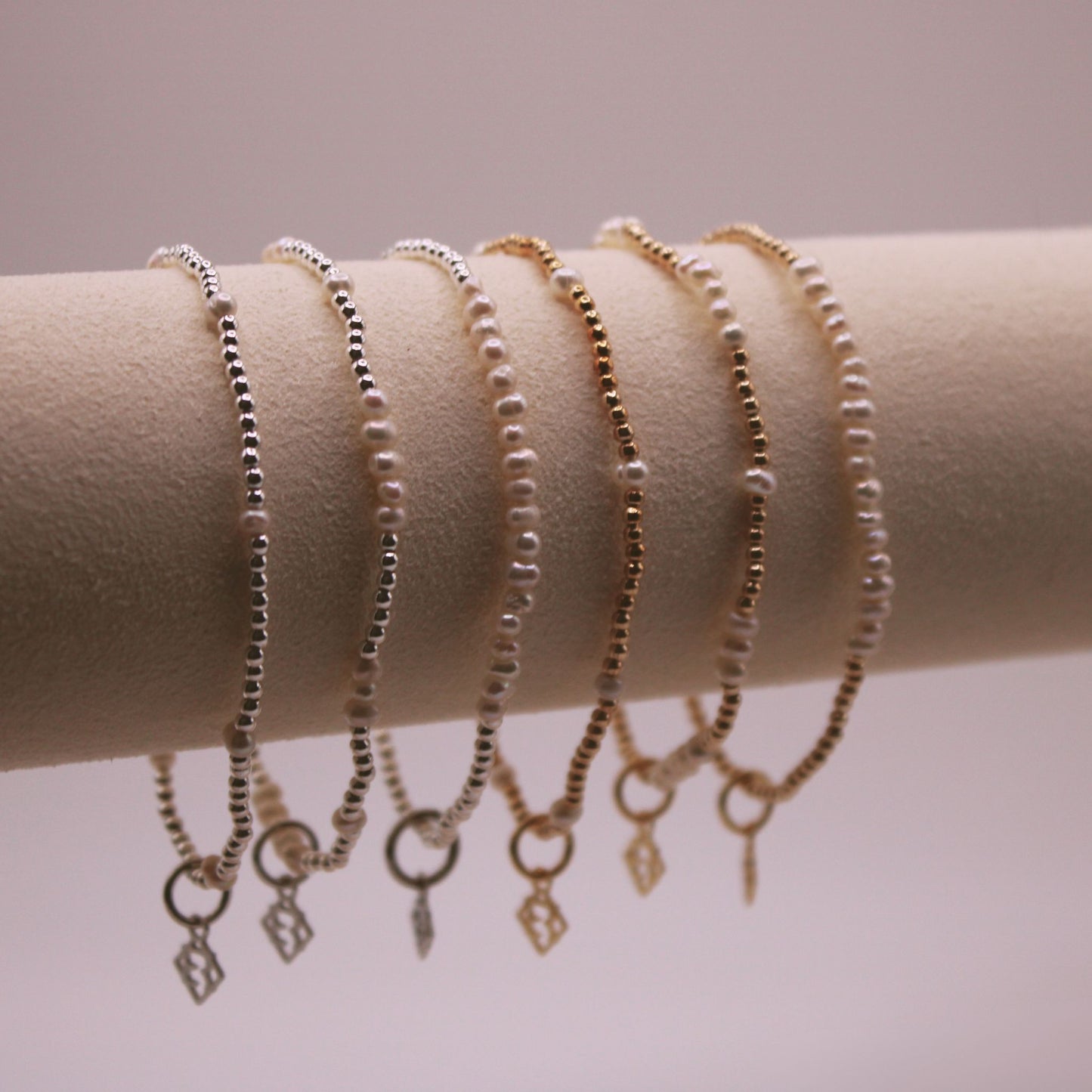 A collection of Radiance Bracelets displayed on a cylindrical surface, featuring beaded chains and small pearl-like elements with different designs.