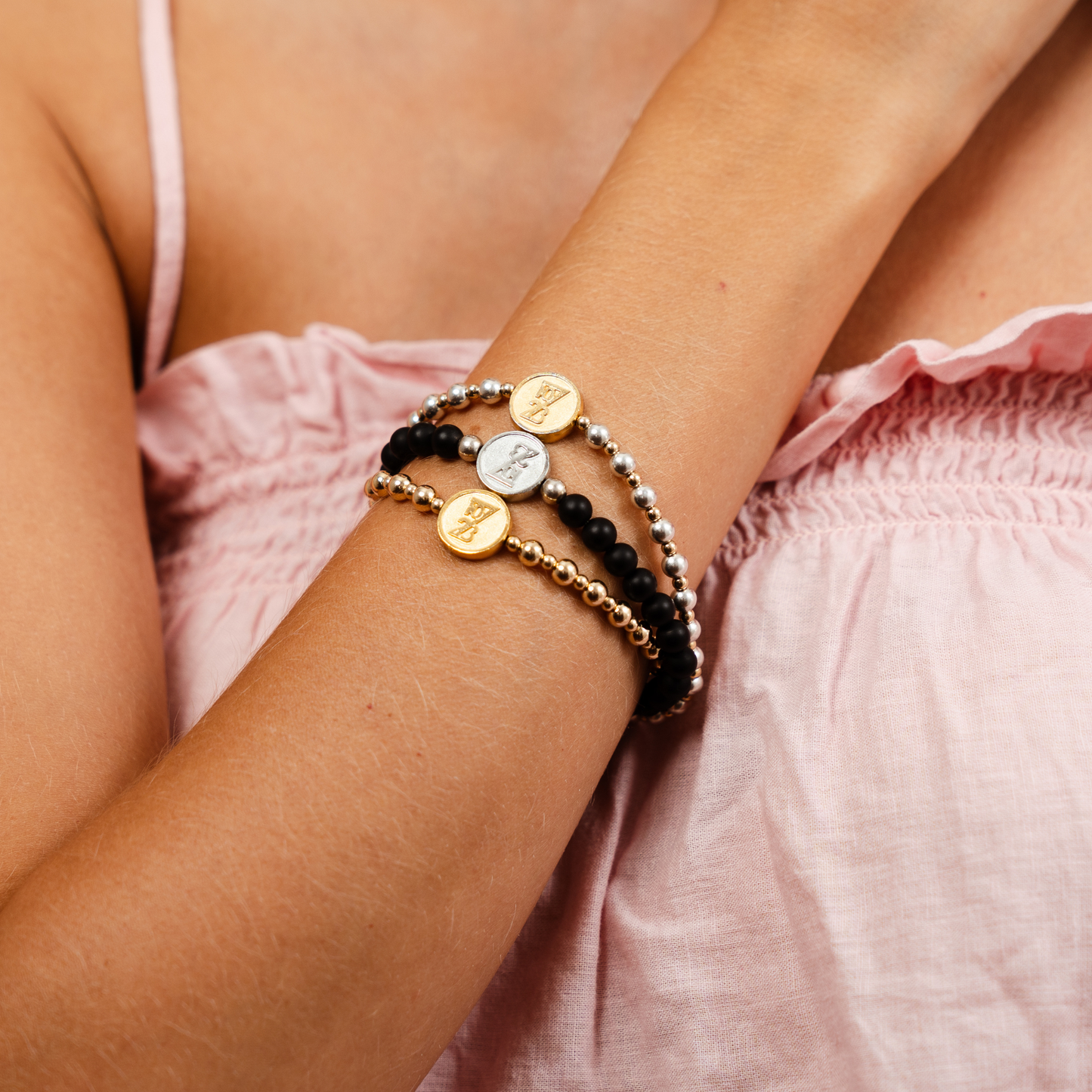 Close-up of a person's wrist wearing multiple bracelets with a pink top.