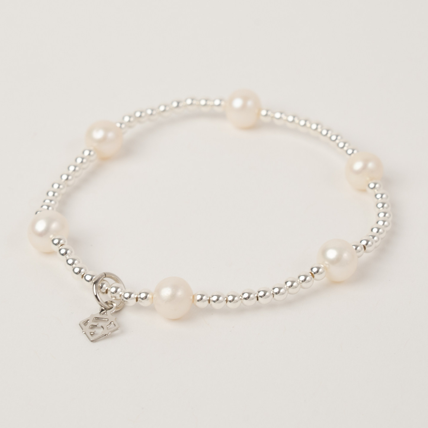 Pearl bracelet with a silver charm on a light gray background