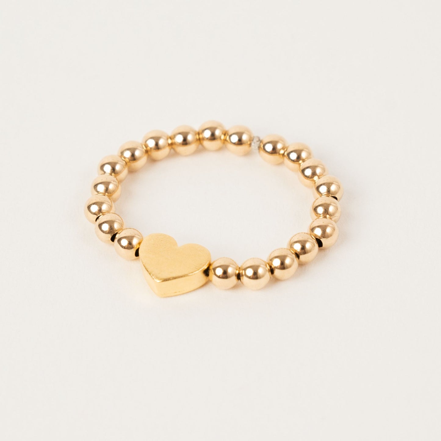 Gold beaded bracelet with a heart charm on a light gray background