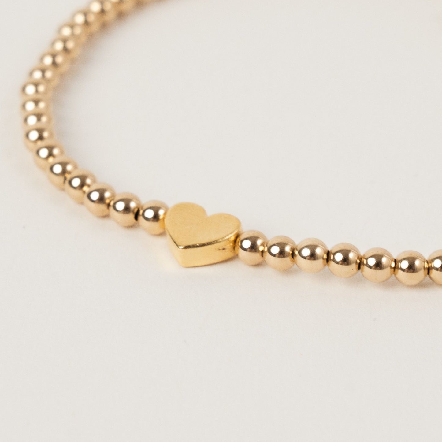 Gold beaded bracelet with a heart charm on a light gray background