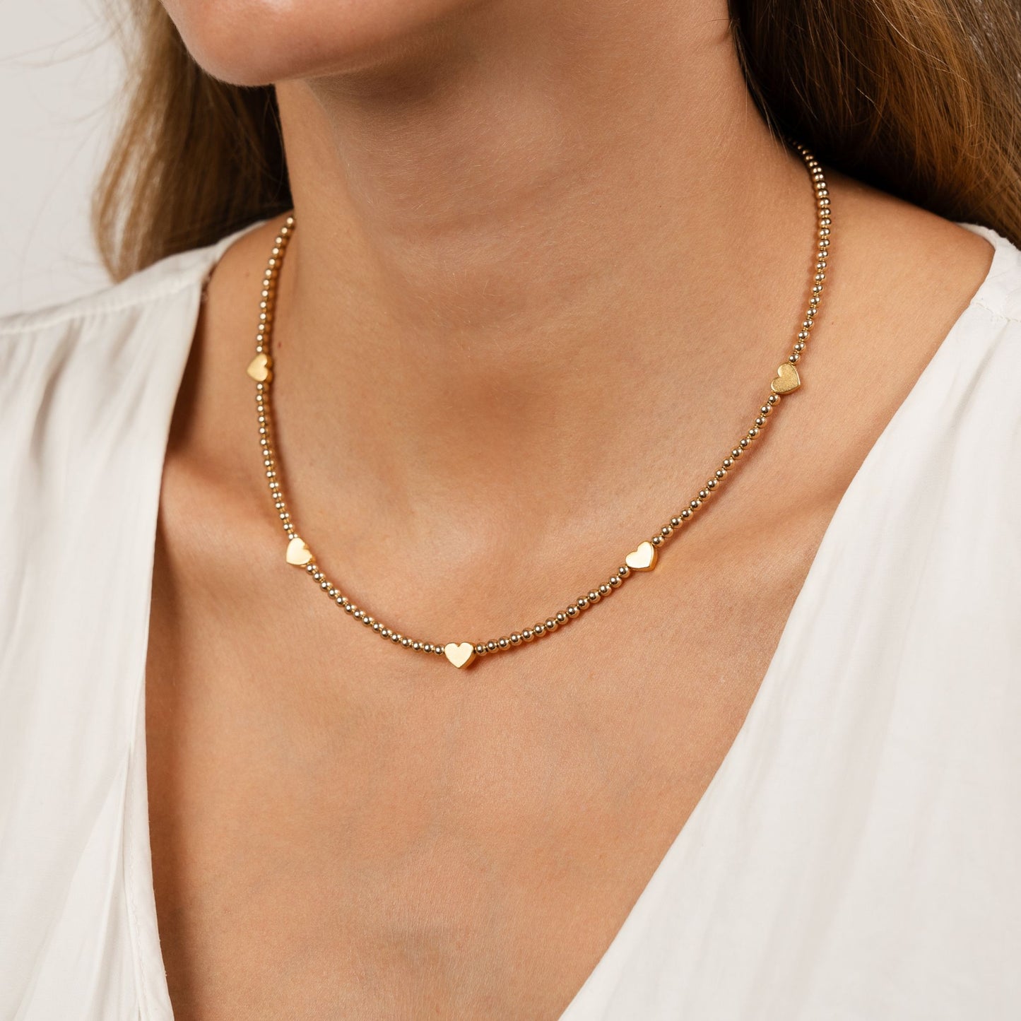 Gold necklace with heart-shaped pendants worn by a person in a white top.
