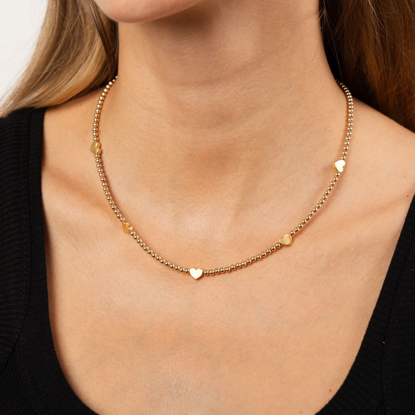 Gold necklace with heart-shaped pendants on a person wearing a black top.