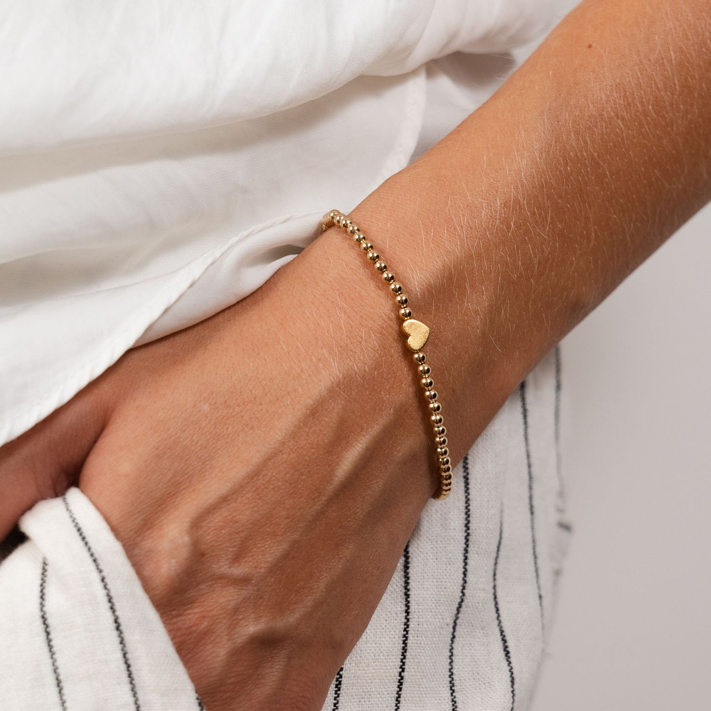 Gold bracelet with a heart charm on a wrist against a white background