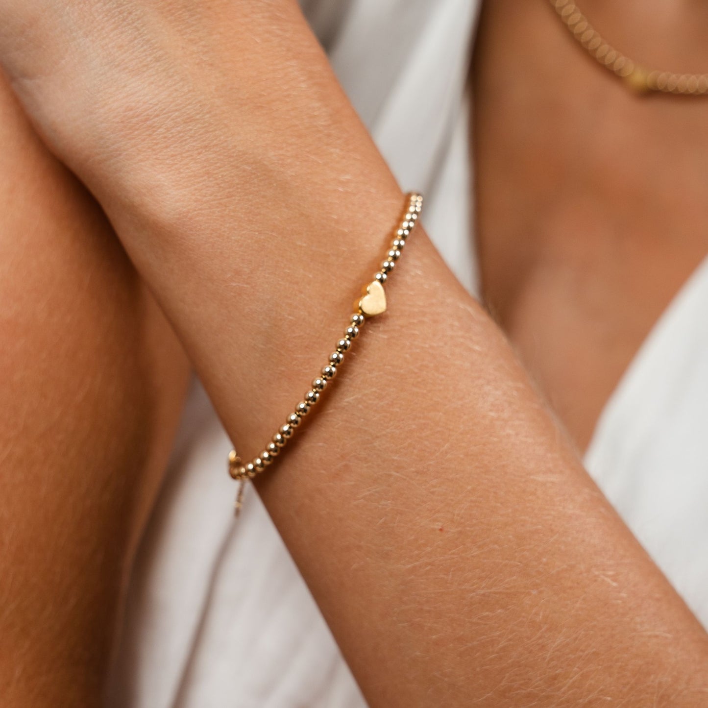 Gold bracelet with a heart charm on a person's wrist against a neutral background