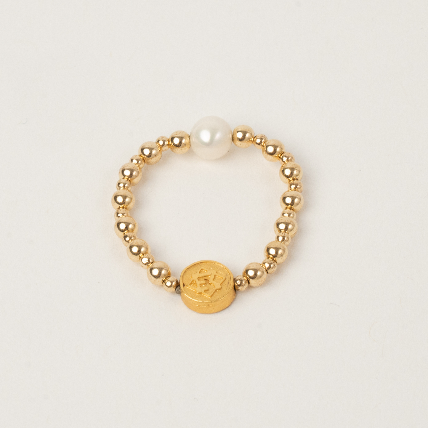 Gold beaded ring with a central round pendant on a light beige background