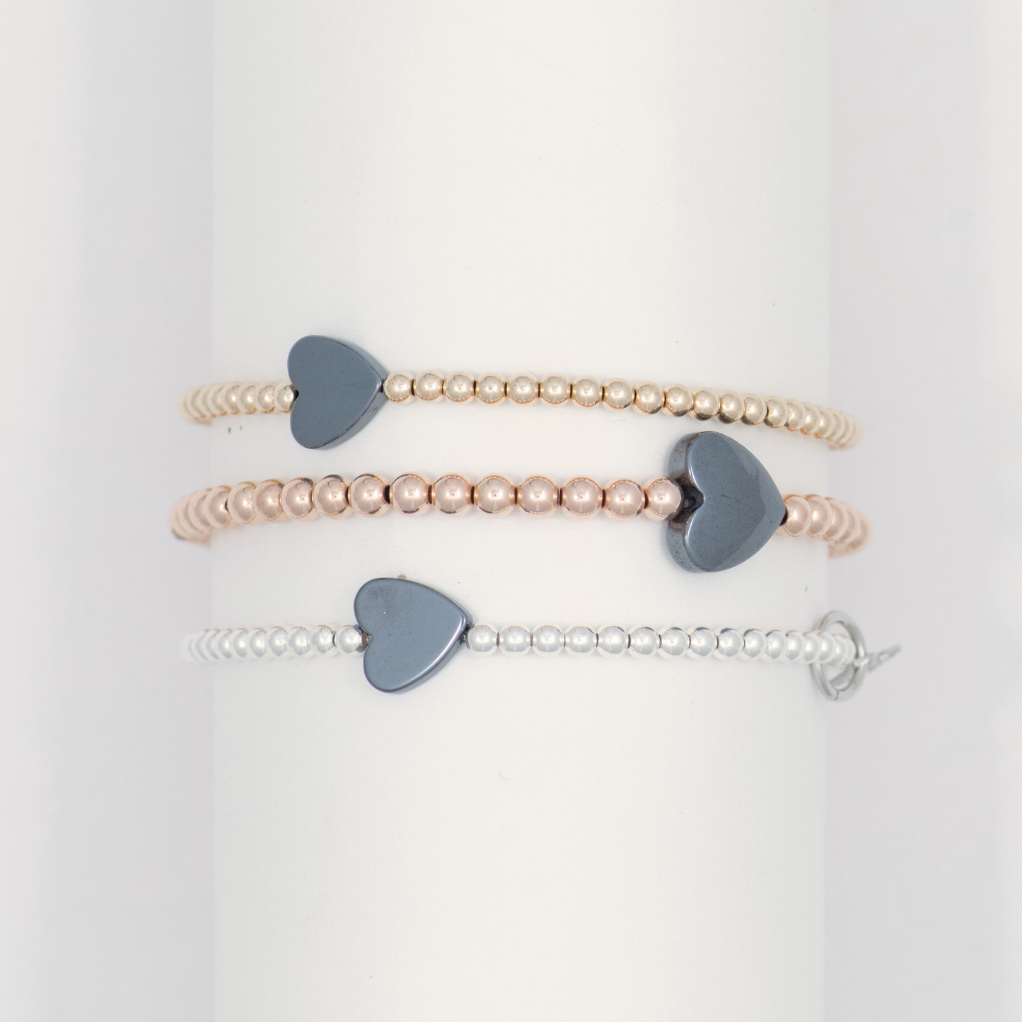 Set of three pearl bracelets with heart-shaped charms on a white background