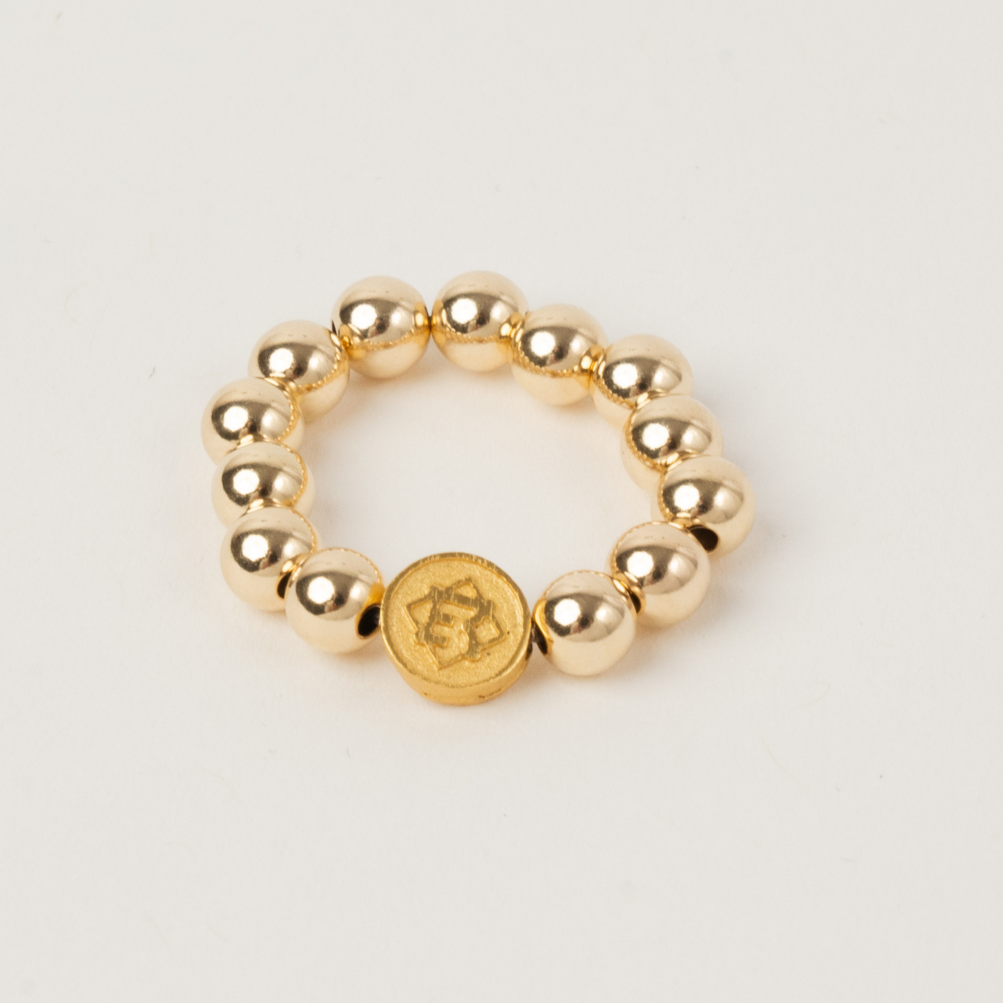 Gold beaded ring with a central coin charm on a light gray background