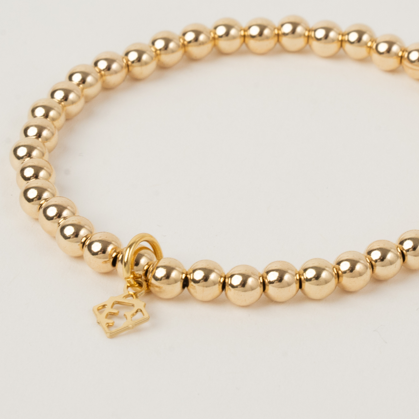 Gold beaded bracelet with a heart charm on a light gray background