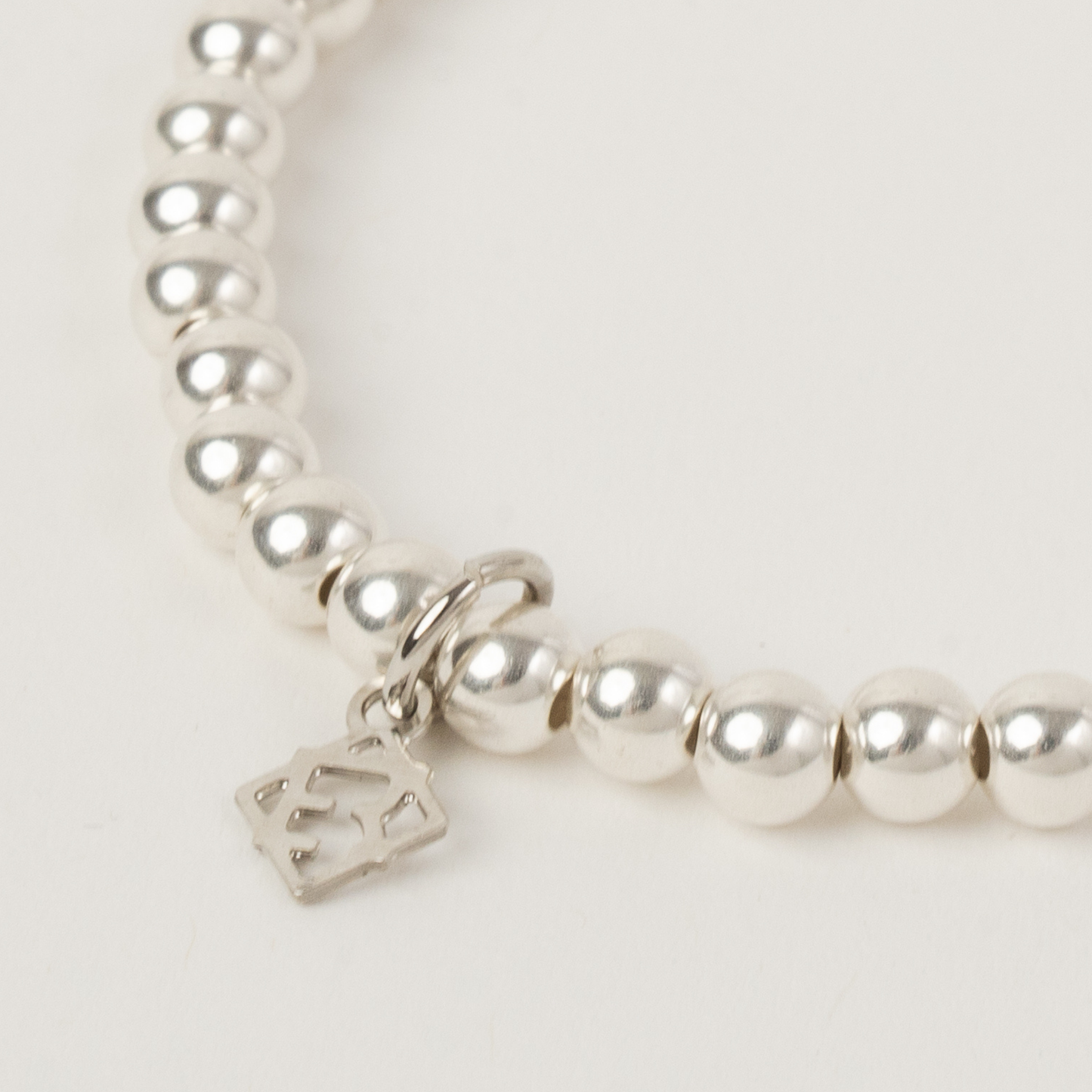 Silver beaded bracelet with a crown charm on a light gray background