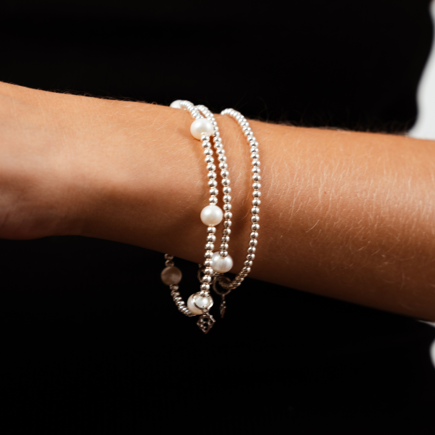 Close-up of a wrist wearing multiple pearl bracelets on a black background