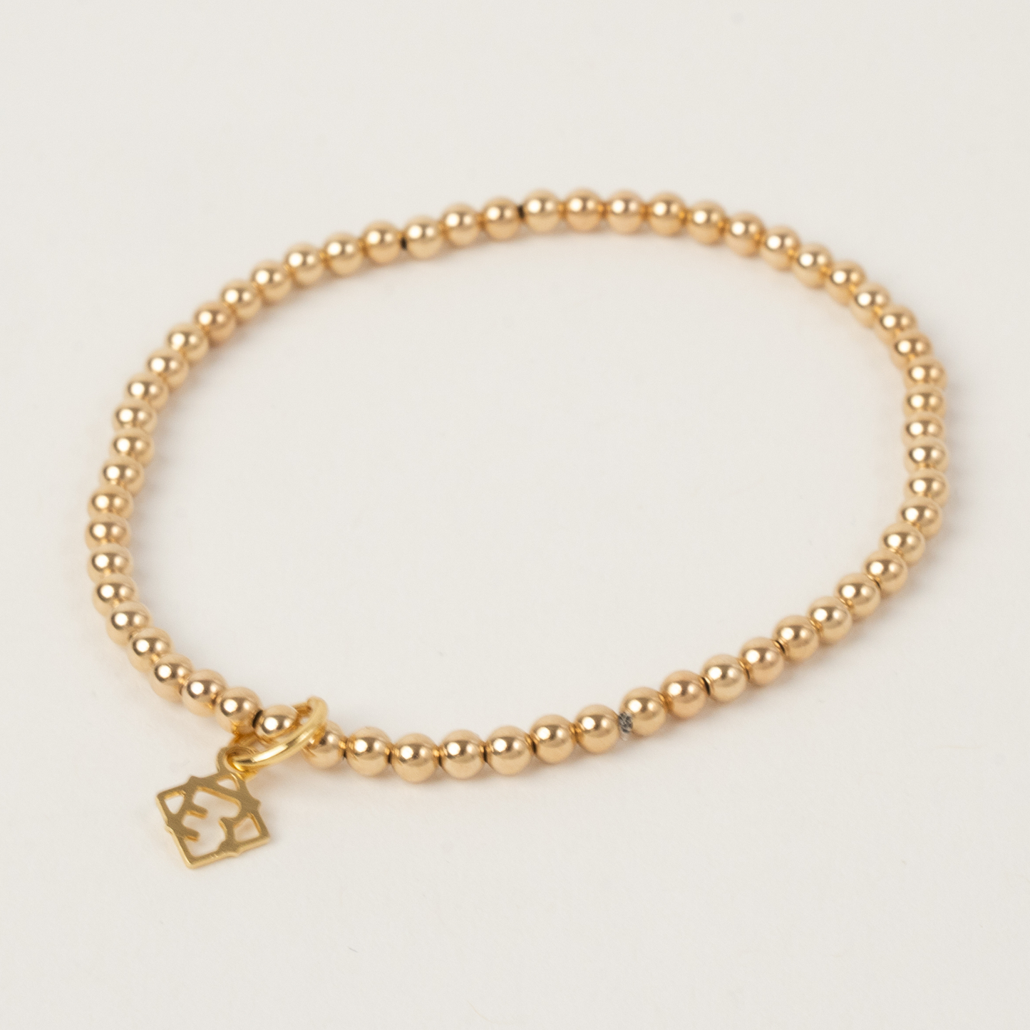 Gold beaded bracelet with a small charm on a light gray background
