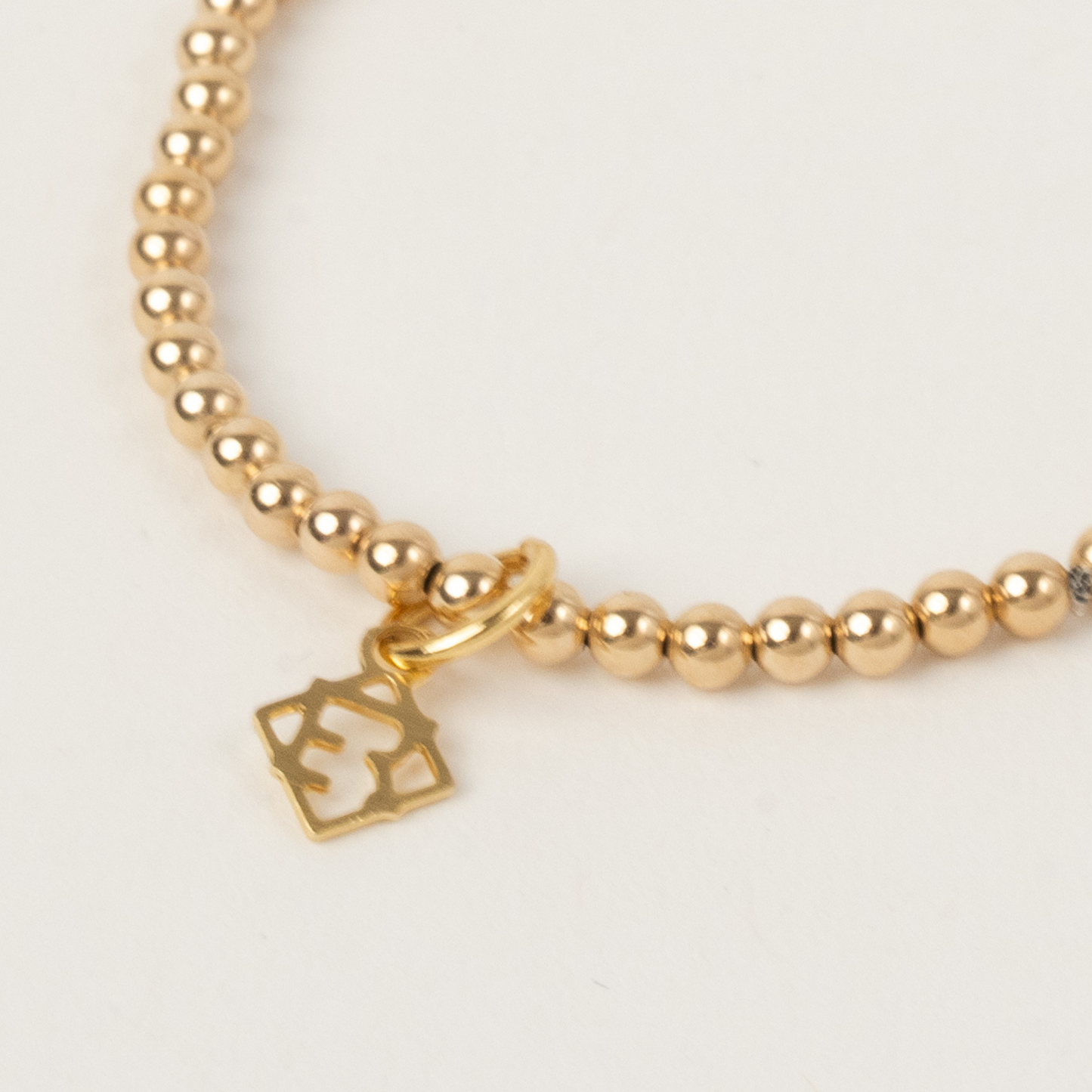 Gold beaded bracelet with a gold charm on a light gray background