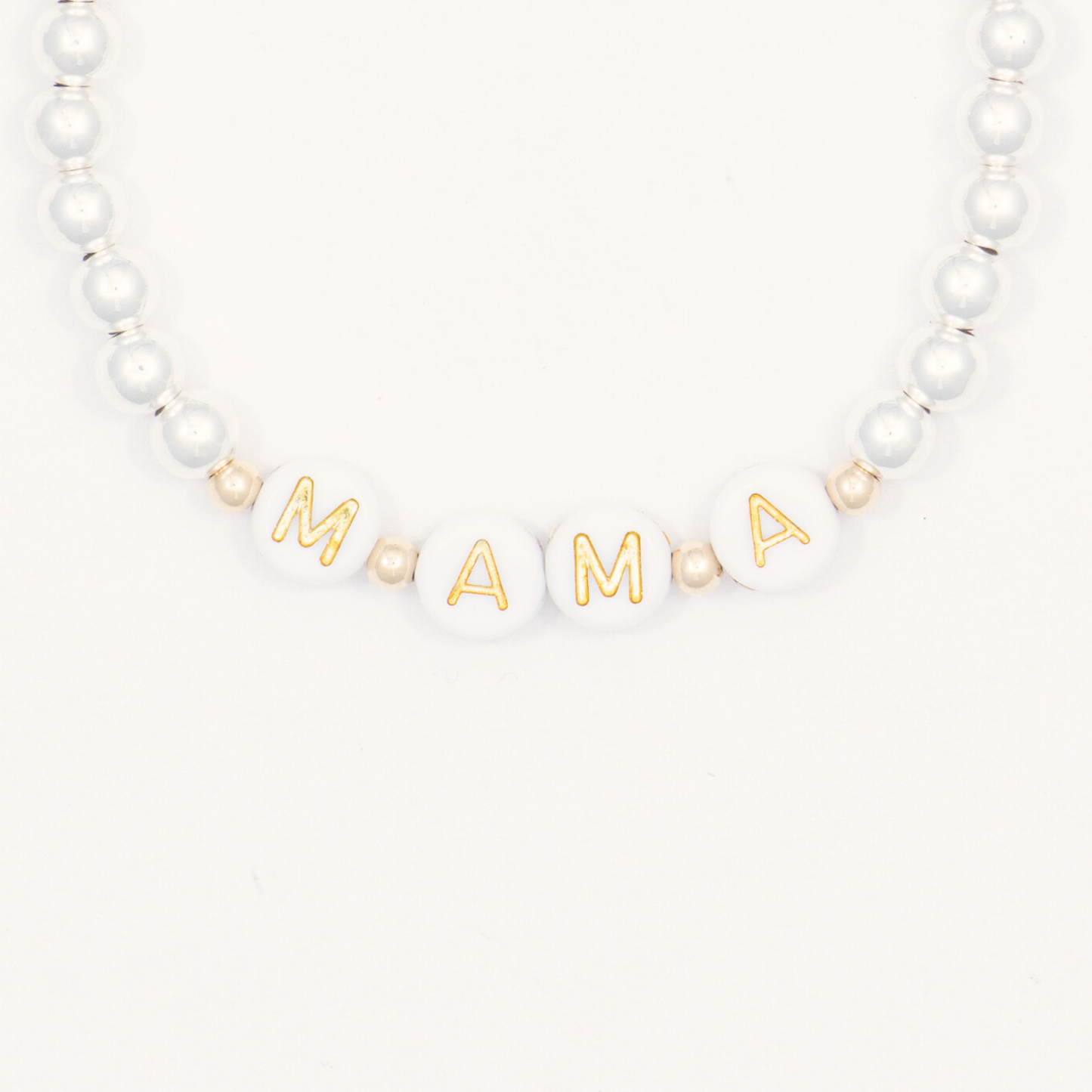 Bracelet with white beads and gold letter beads spelling 'MAMA' on a white background
