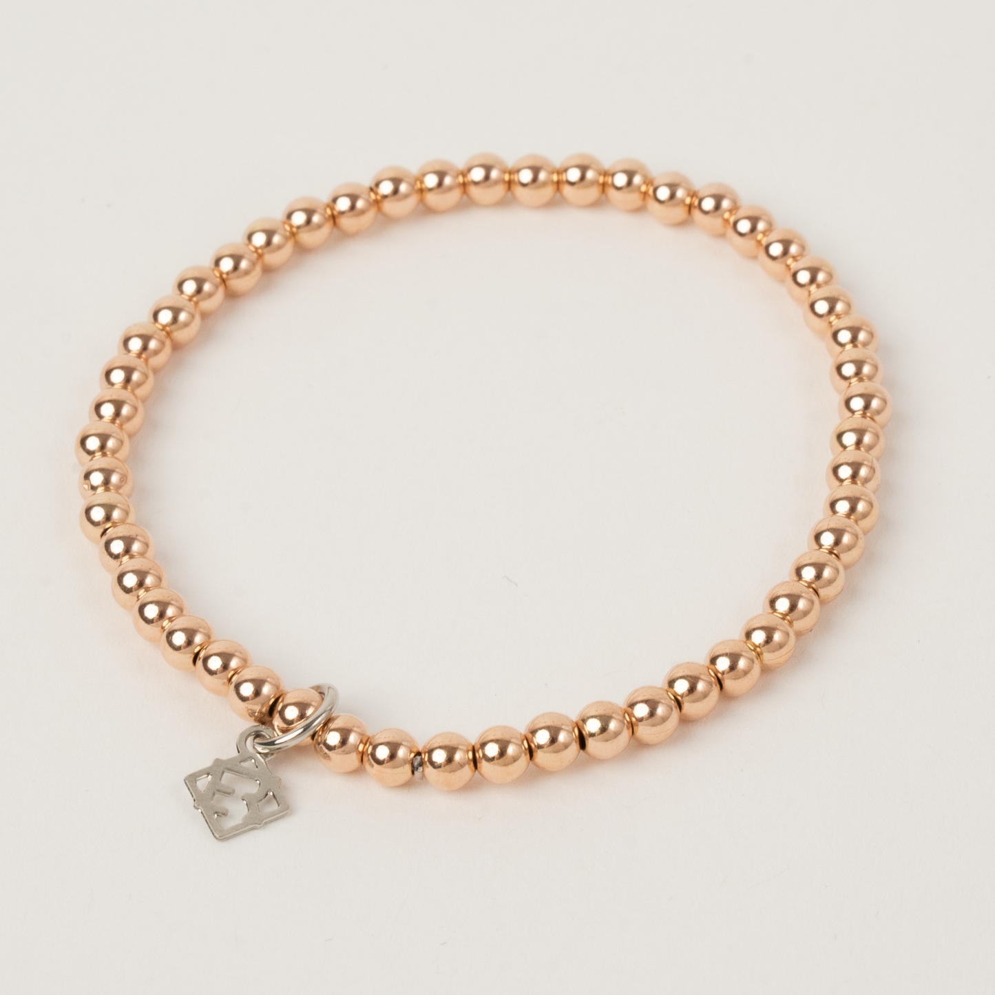 Rose gold beaded bracelet with a silver tag on a light gray background