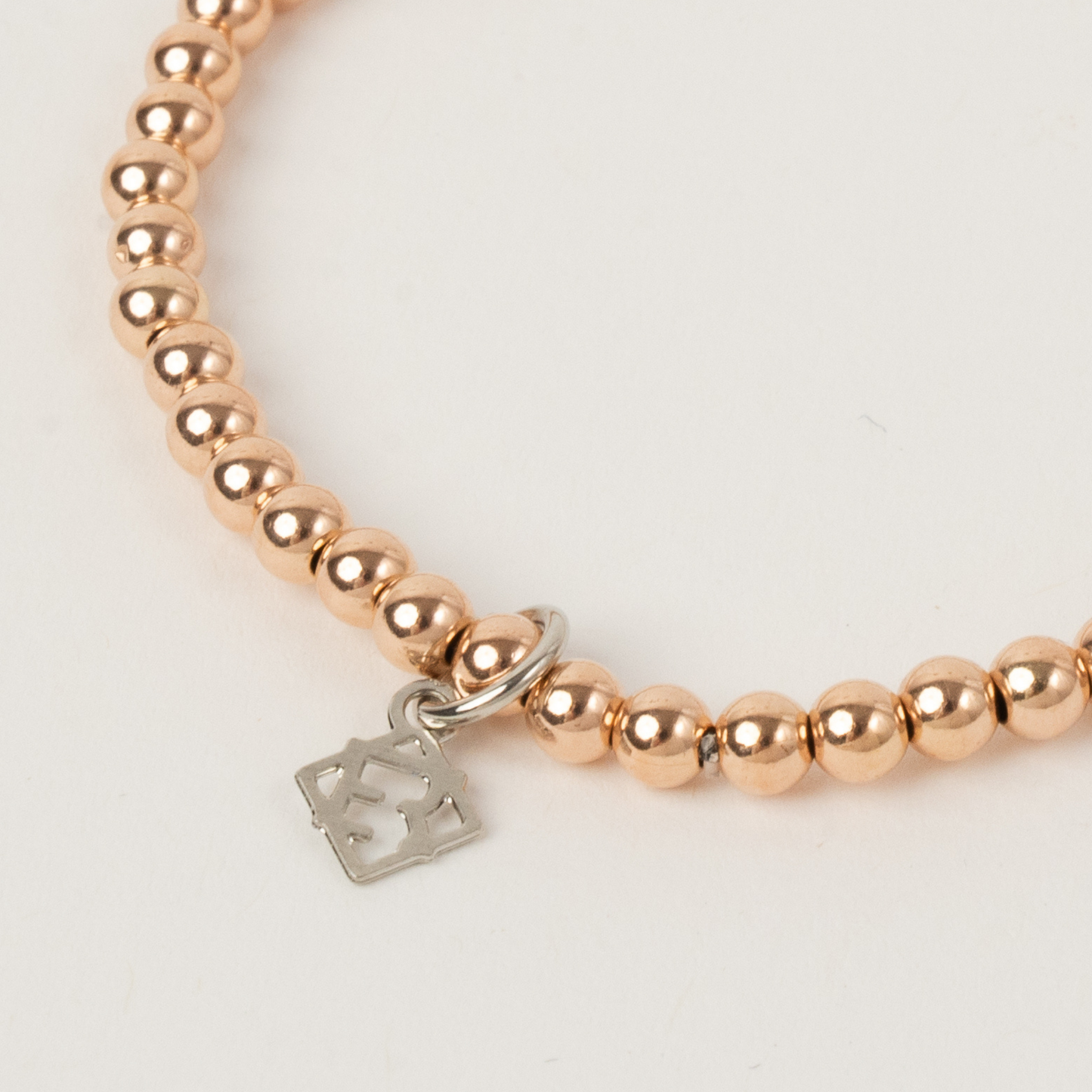 Rose gold beaded bracelet with a silver tag on a light background