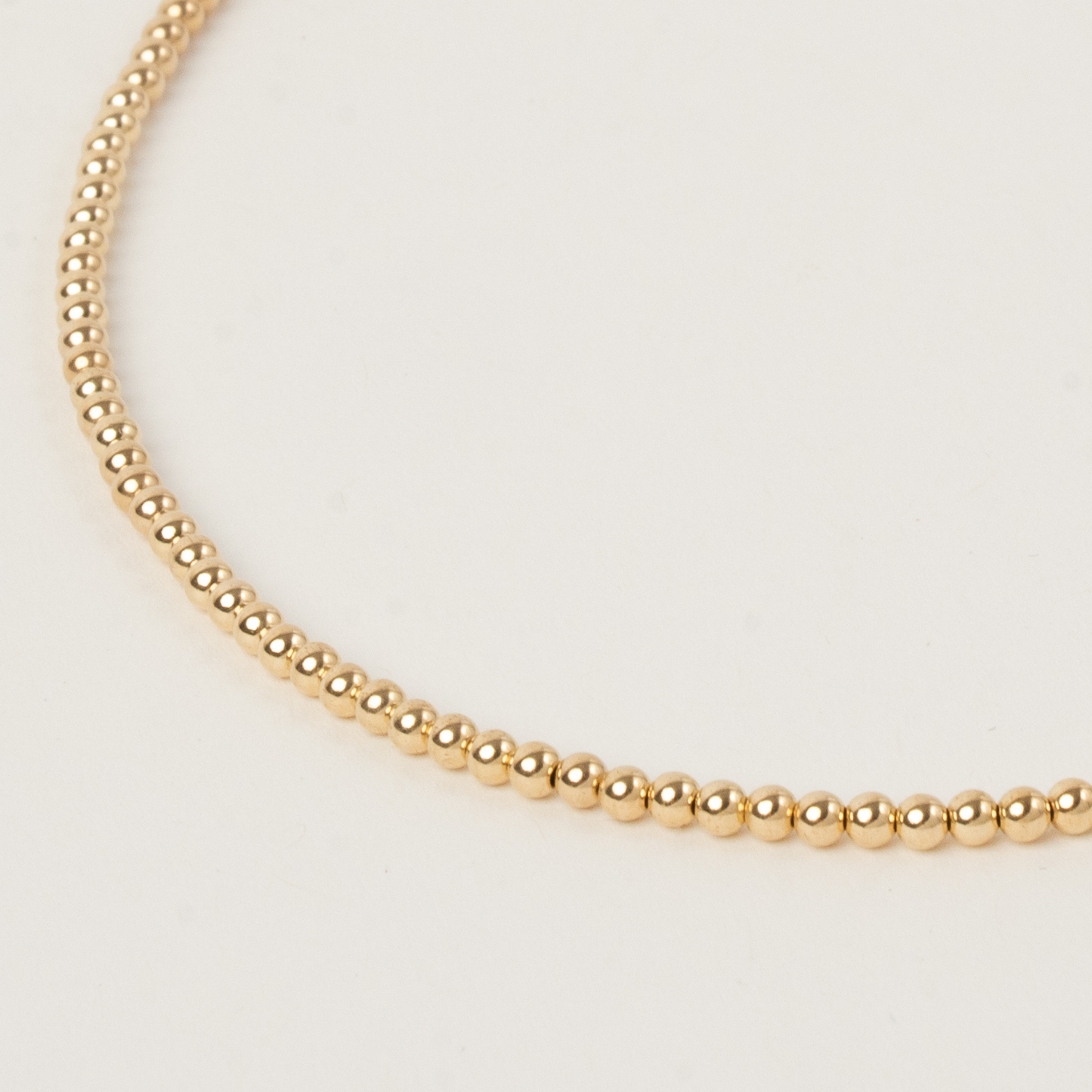 Gold beaded necklace on a light beige background
