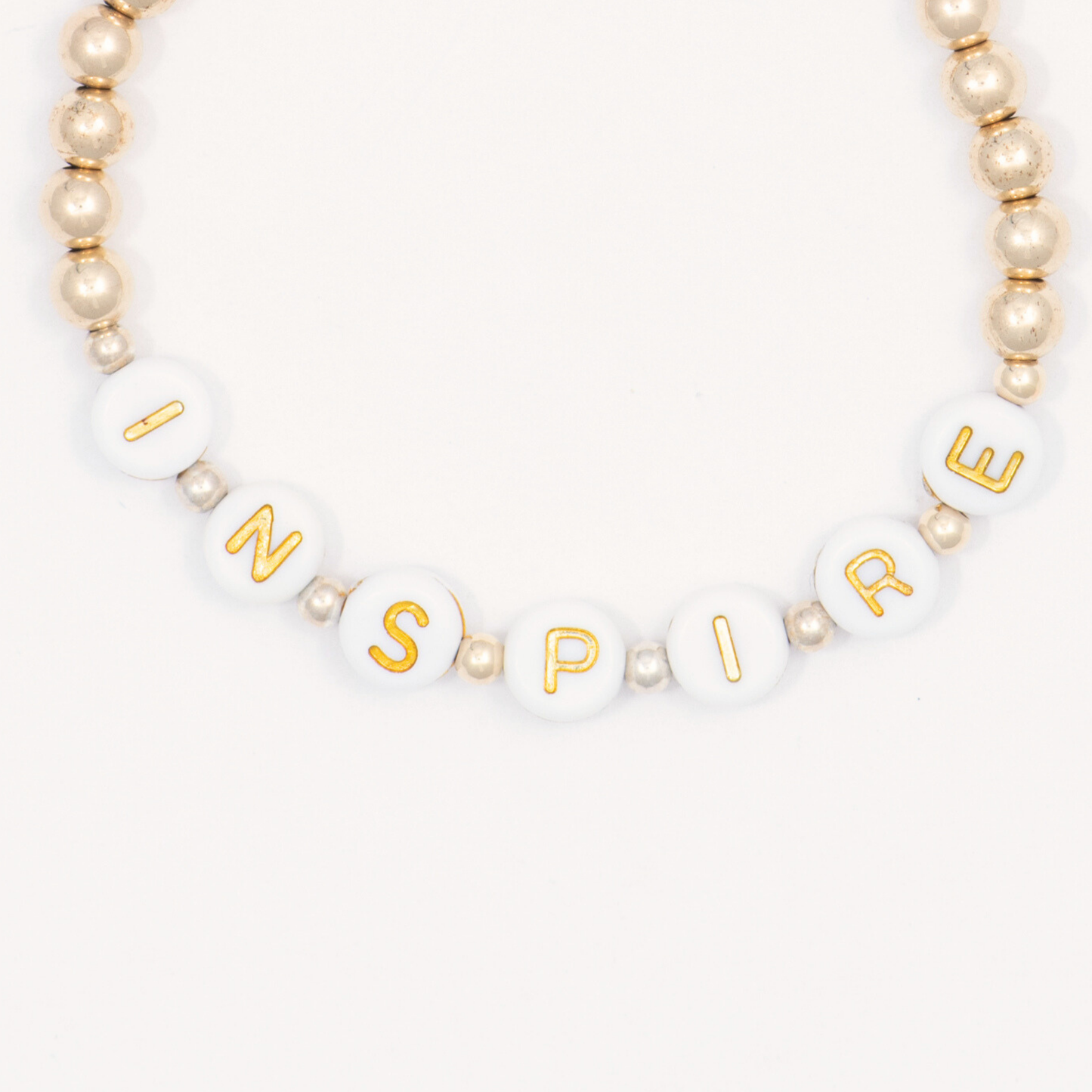 Bracelet with gold letter beads spelling 'INSPIRE' on a white background