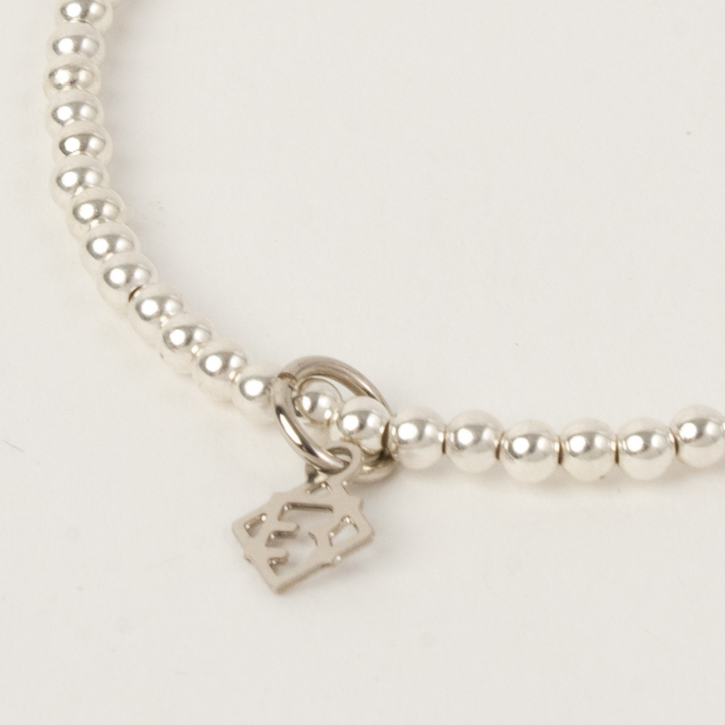 Silver beaded bracelet with a heart-shaped tag on a light gray background