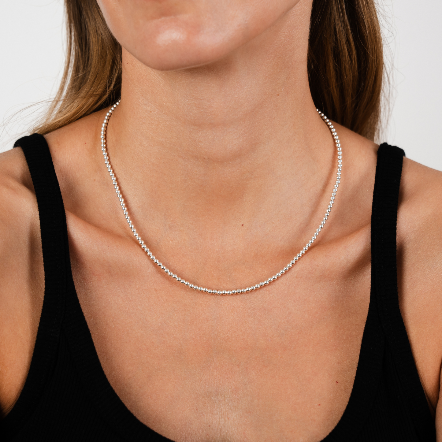 Close-up of a woman wearing a silver necklace against a neutral background