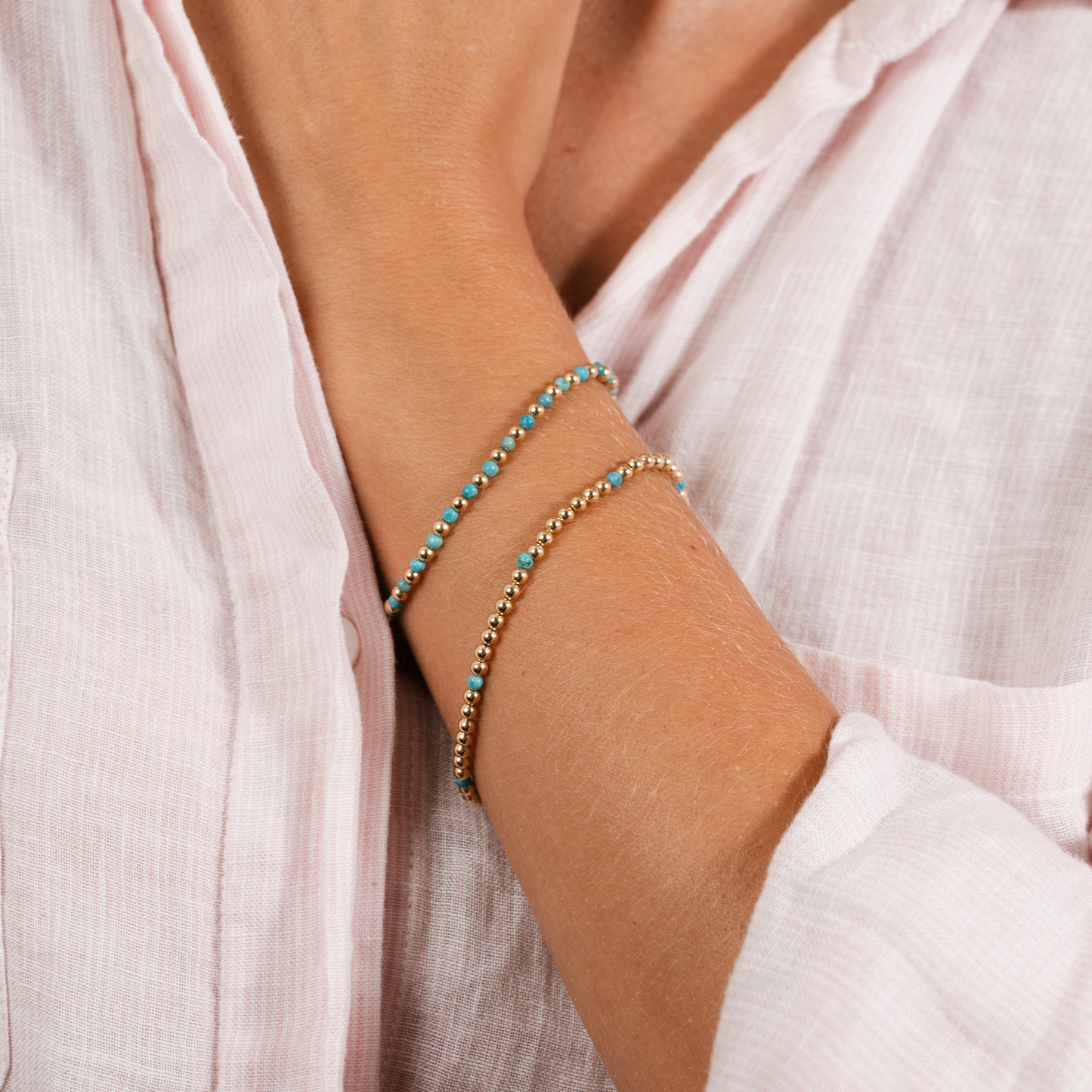 Close-up of a person wearing two bracelets on a light pink background