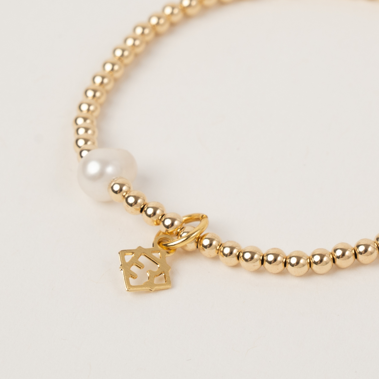 Gold beaded bracelet with a heart-shaped charm on a light background