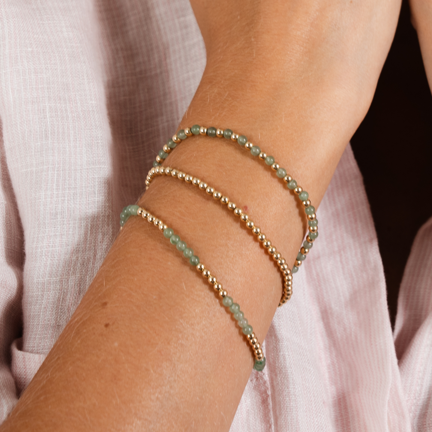 Close-up of a wrist wearing two beaded bracelets on a light pink fabric background
