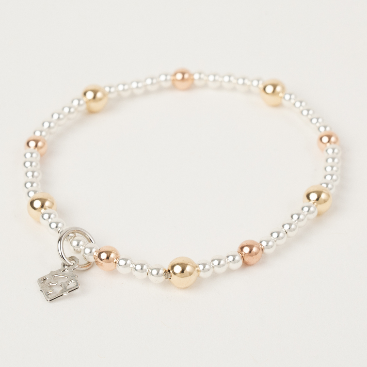 Pearl and gold beaded bracelet with a silver charm on a light gray background