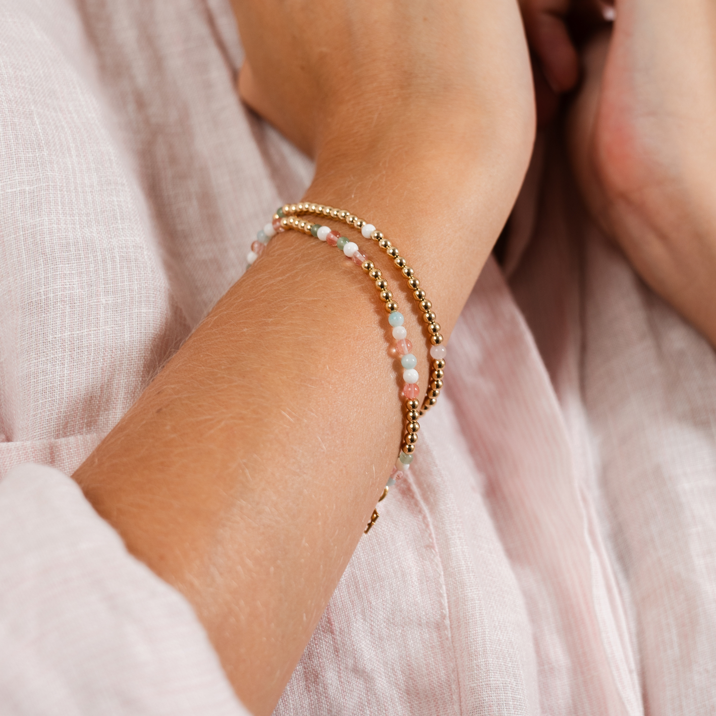 Close-up of a wrist wearing a beaded bracelet with a soft pink background