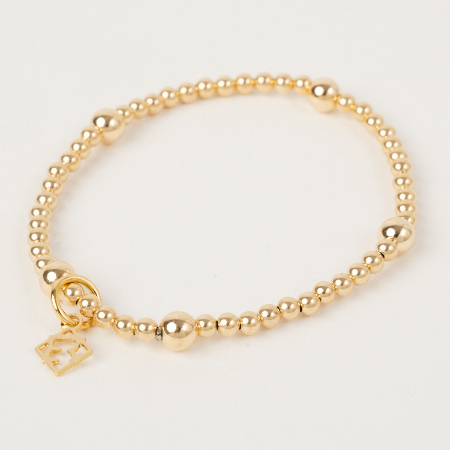 Gold beaded bracelet with a heart-shaped charm on a light gray background