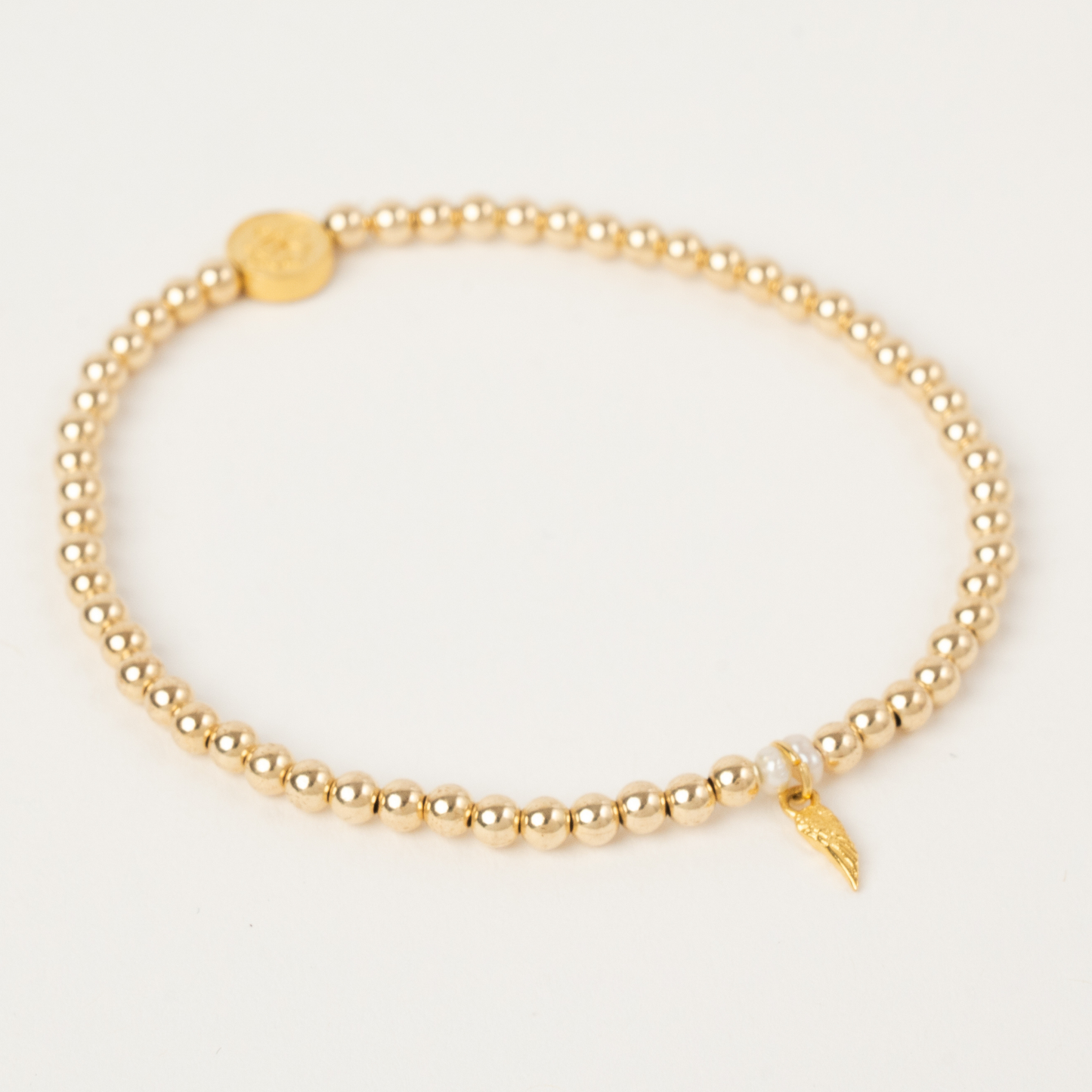 Gold beaded bracelet with a small charm on a light gray background