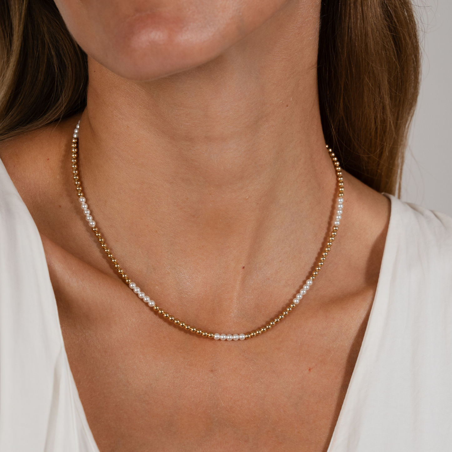 Close-up of a person wearing a gold and pearl necklace against a neutral background