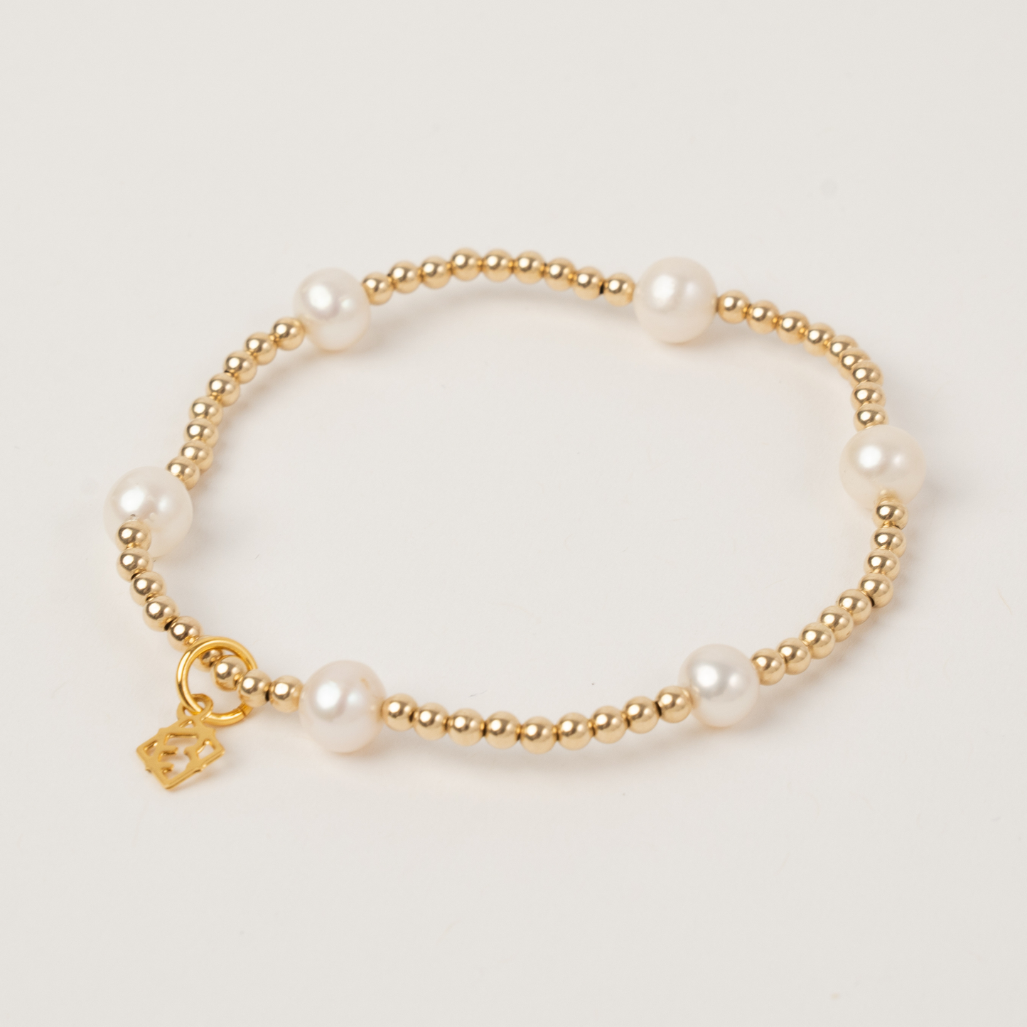 Pearl bracelet with gold beads and a gold tag on a light beige background