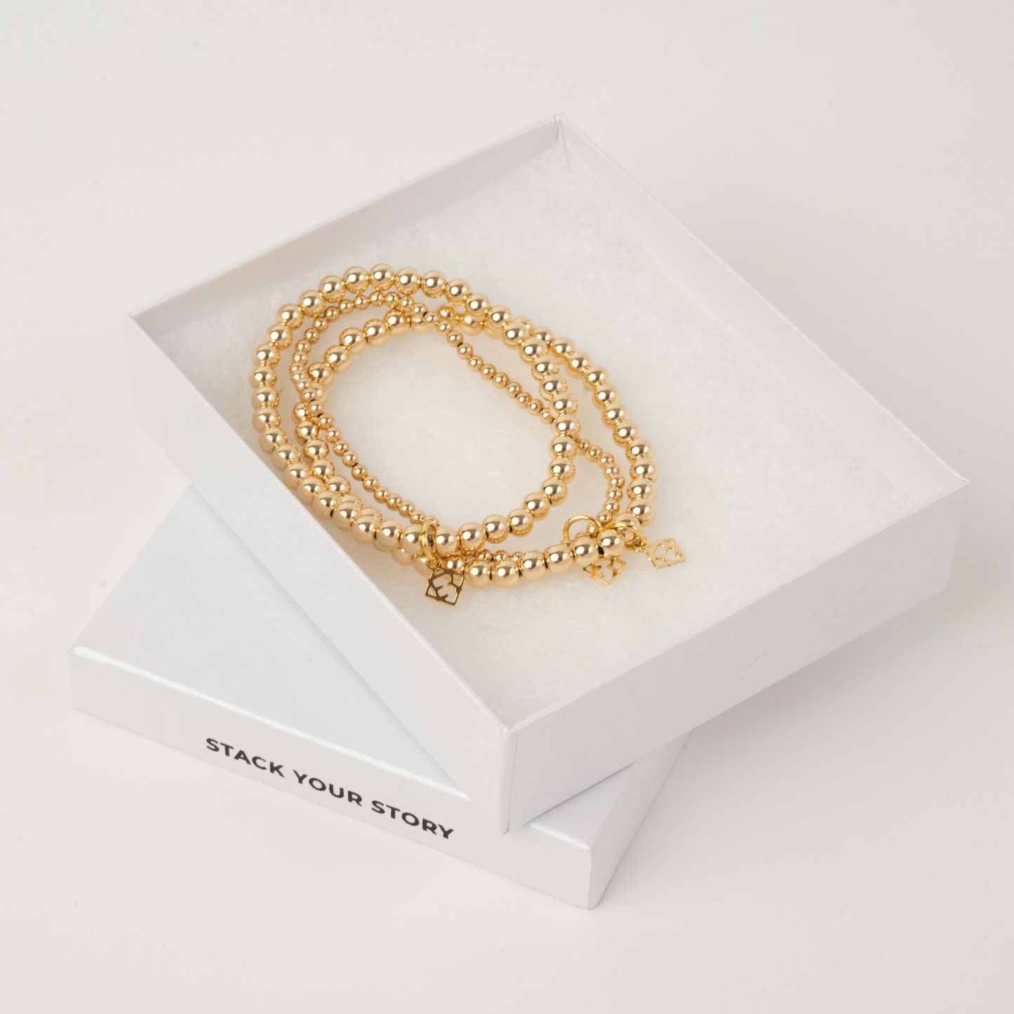 Gold bracelets on a white box with 'Stack Your Story' text