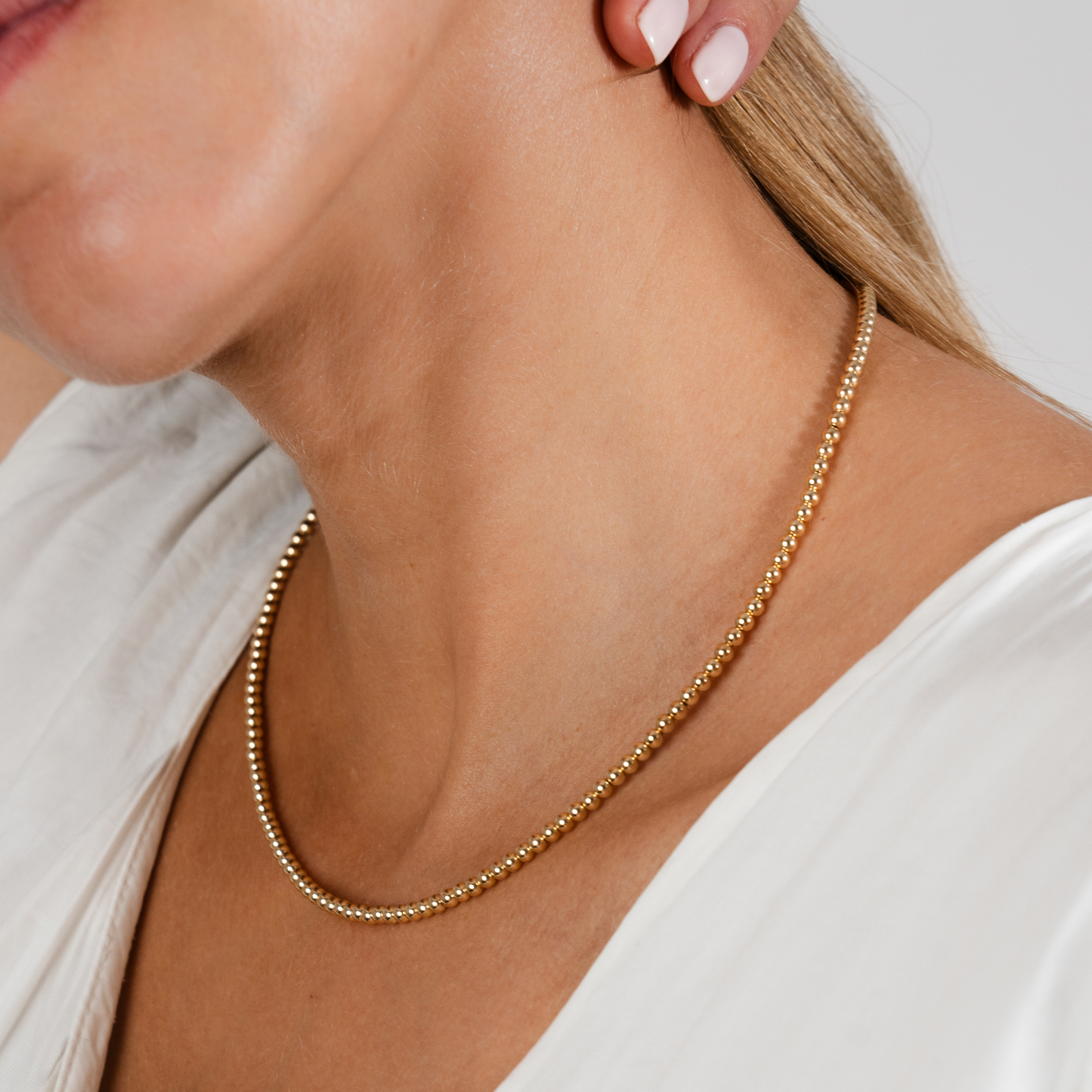 Gold necklace worn by a person with a neutral background