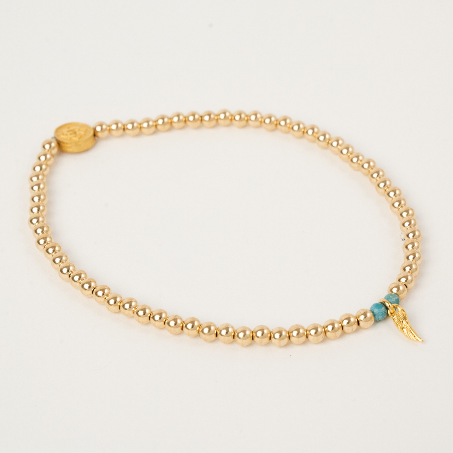 Gold beaded bracelet with a turquoise bead on a light gray background