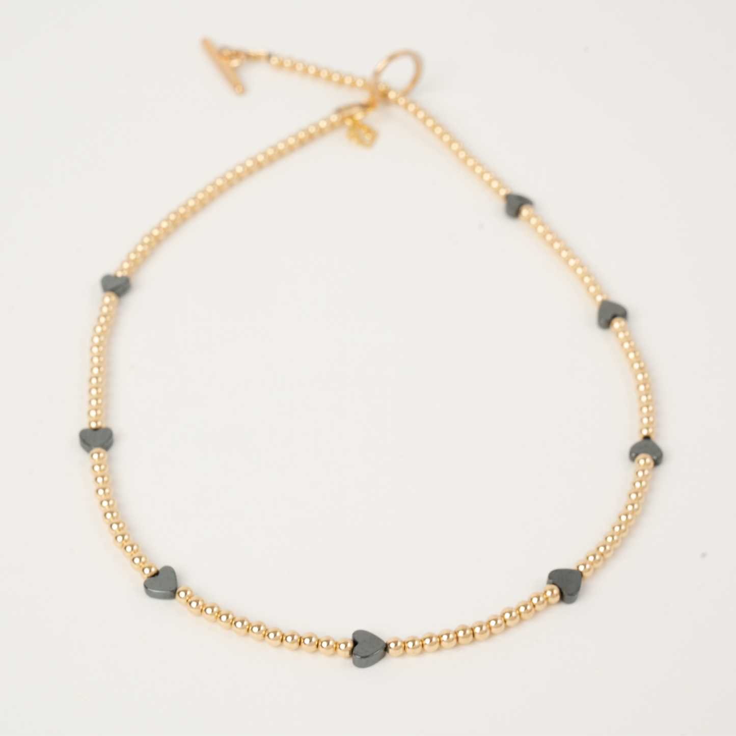 Gold necklace with gray heart-shaped beads on a light gray background