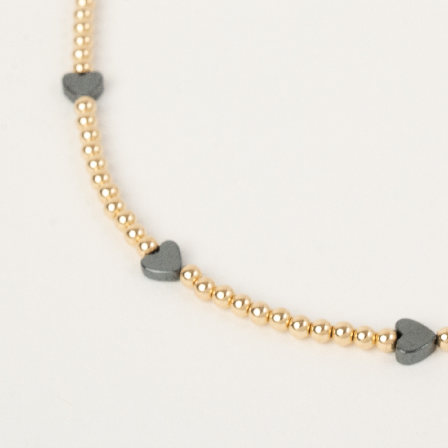 Necklace with gold beads and heart-shaped gray charms on a light gray background