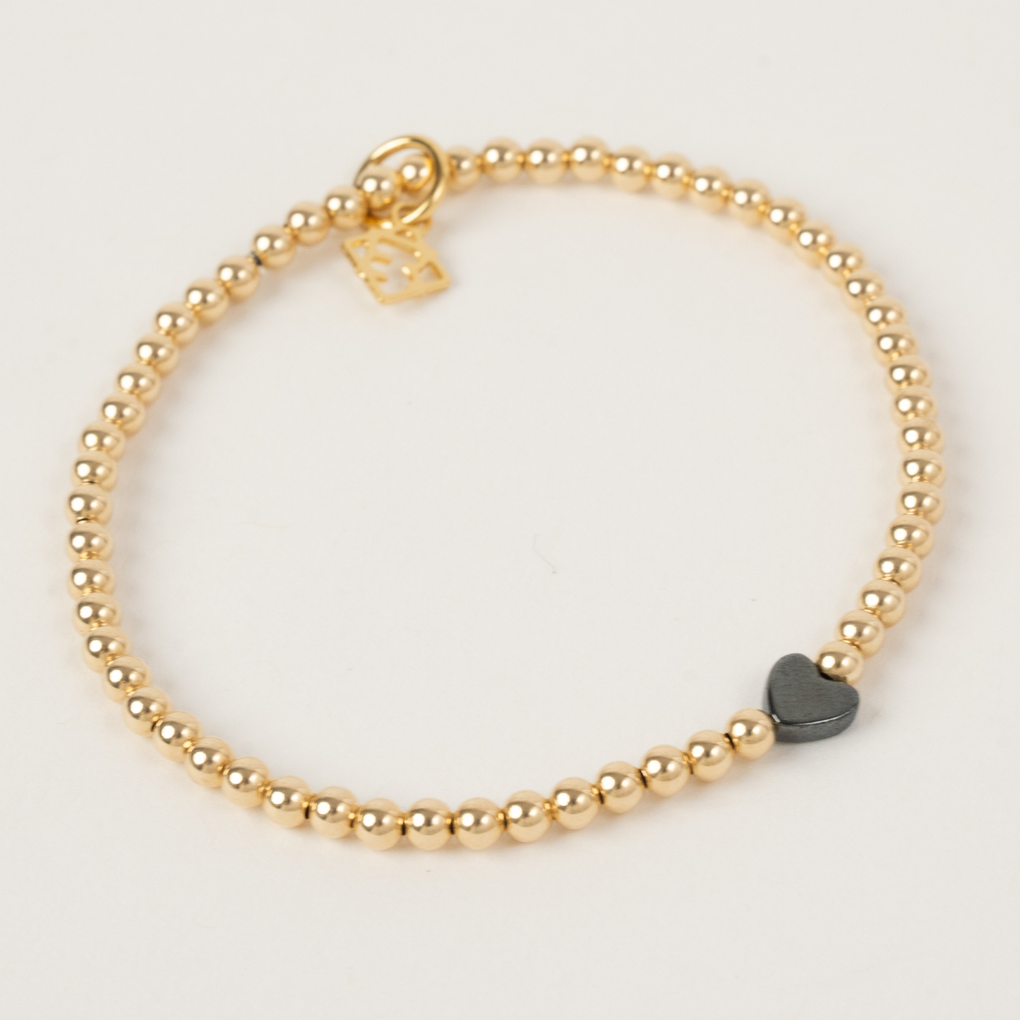 Gold beaded bracelet with a heart-shaped charm on a light gray background