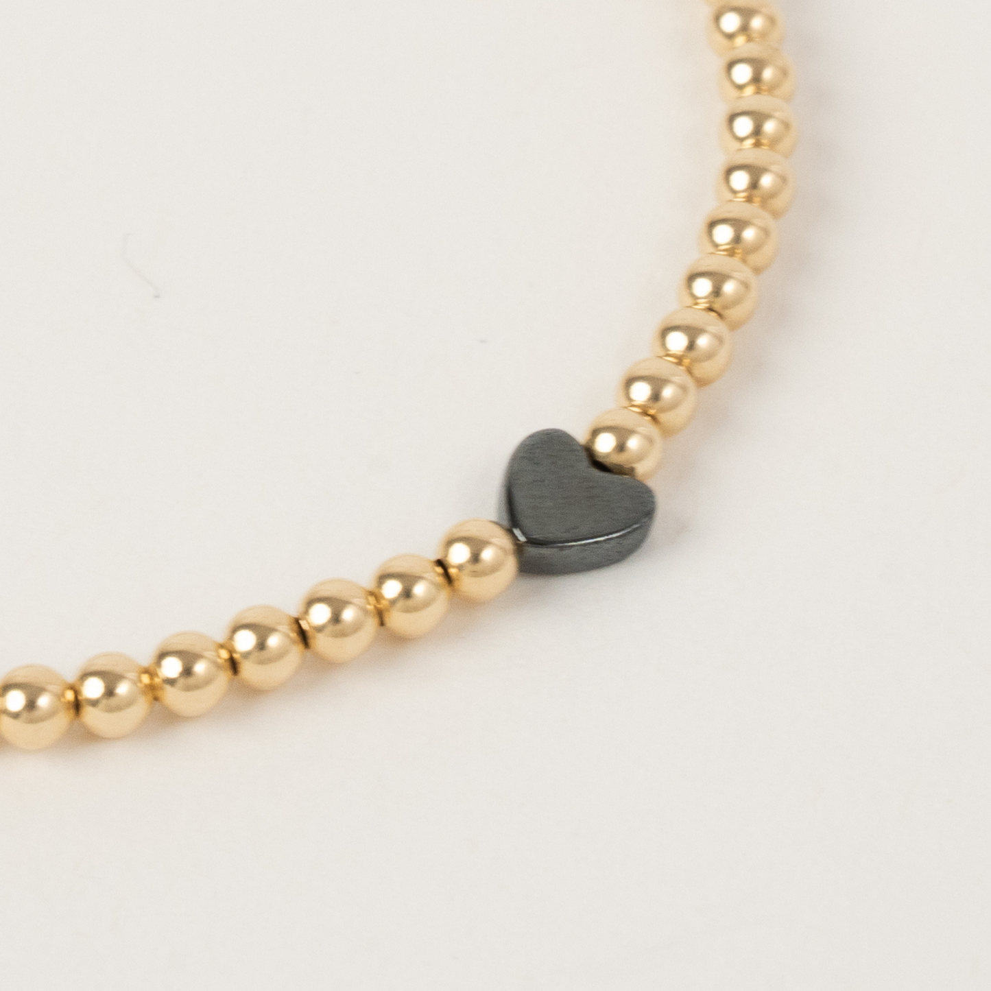 Gold beaded bracelet with a heart-shaped charm on a light background