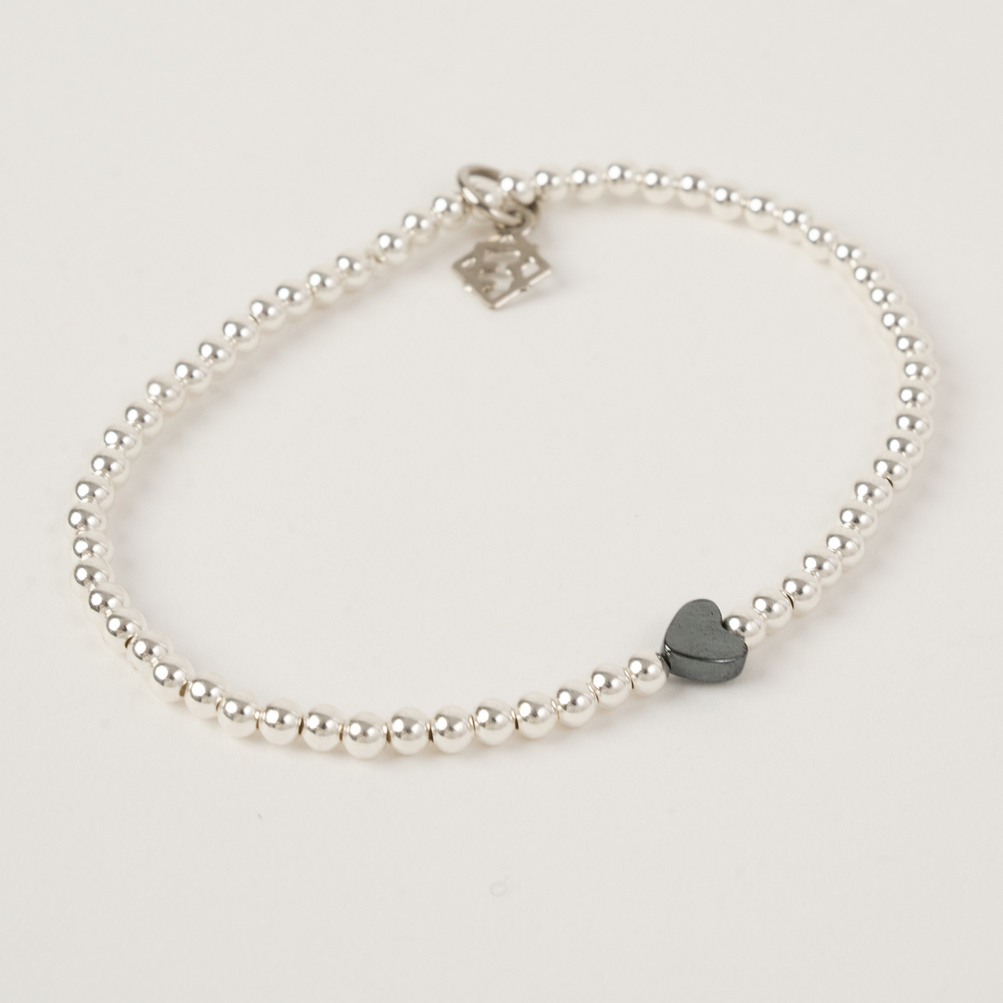 Silver beaded bracelet with a heart-shaped charm on a light gray background
