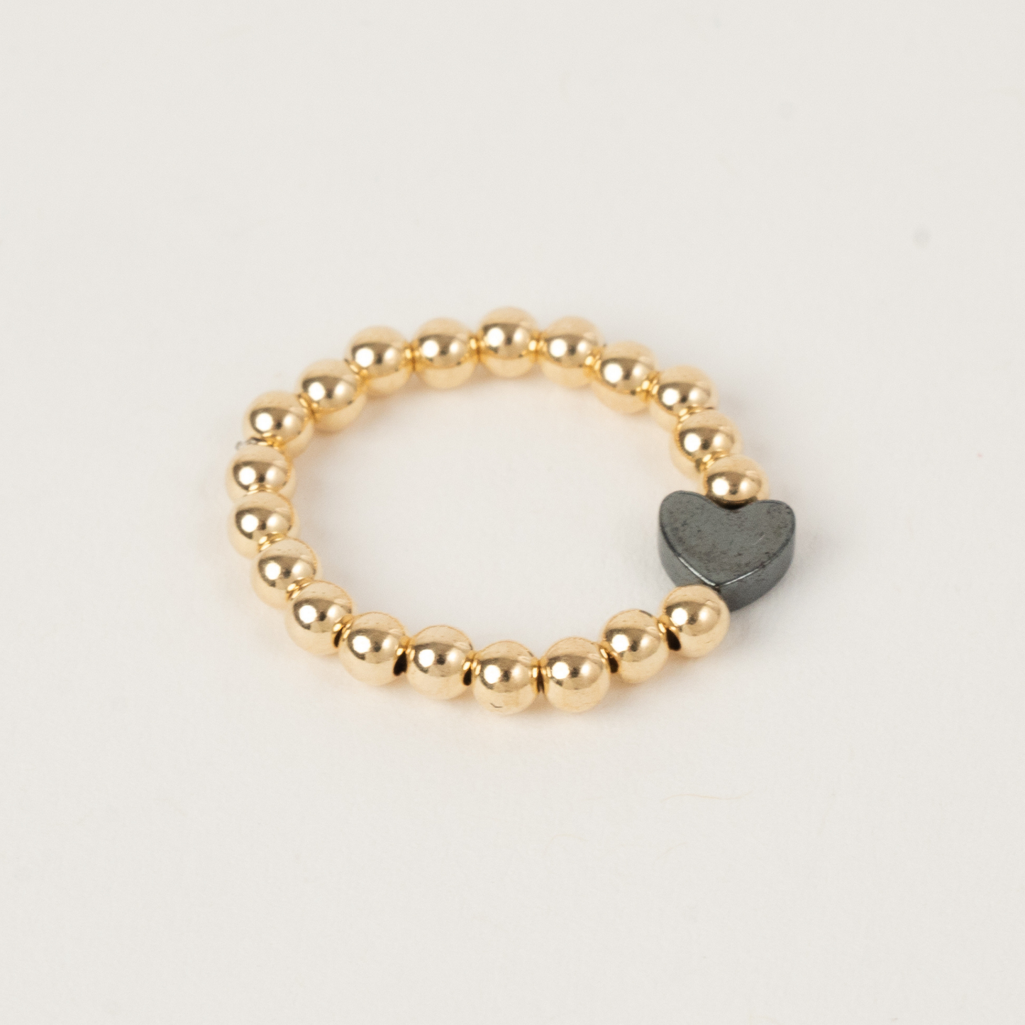 Gold beaded ring with a gray heart charm on a white background
