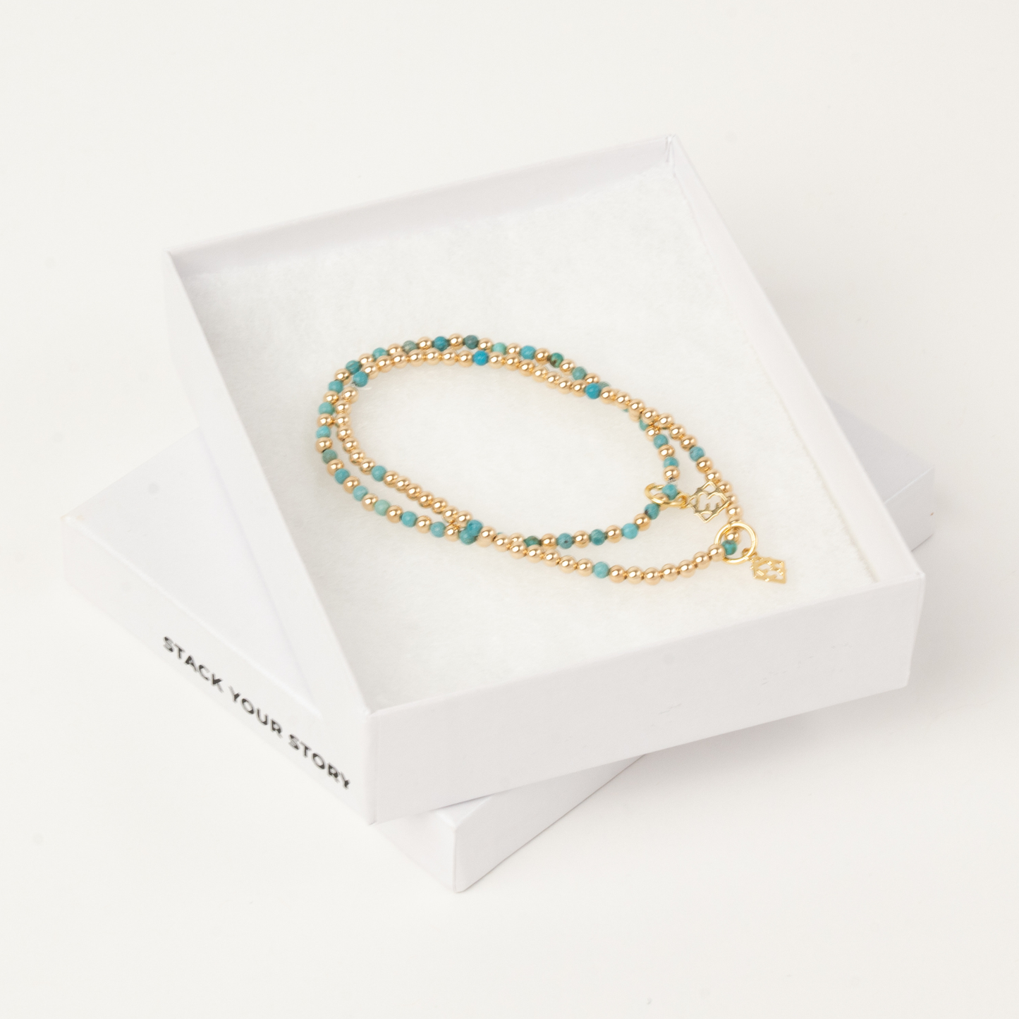 Gold bracelet with turquoise beads on a white card with 'Stack Your Story' branding.