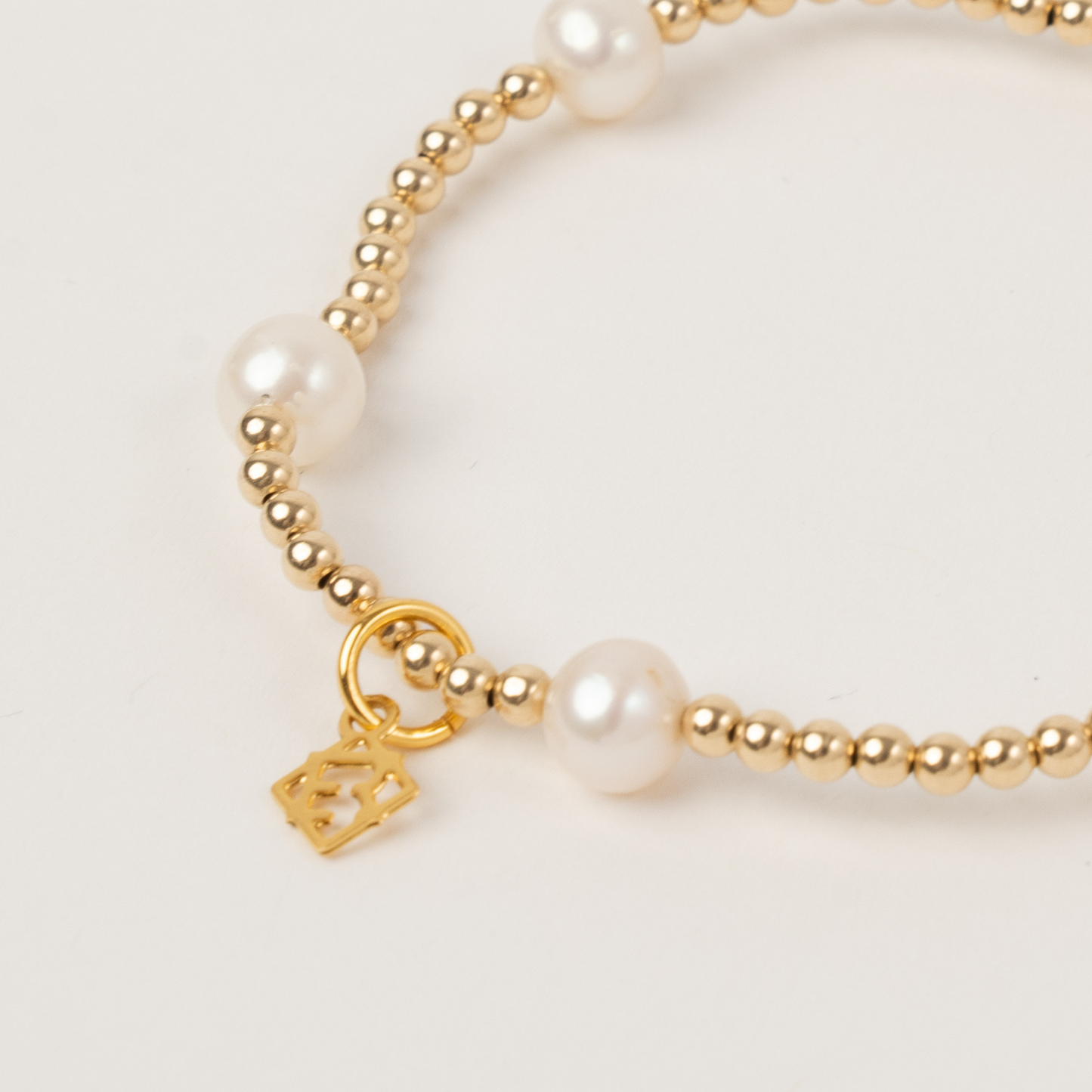 Gold bracelet with pearl beads and a gold charm on a light background